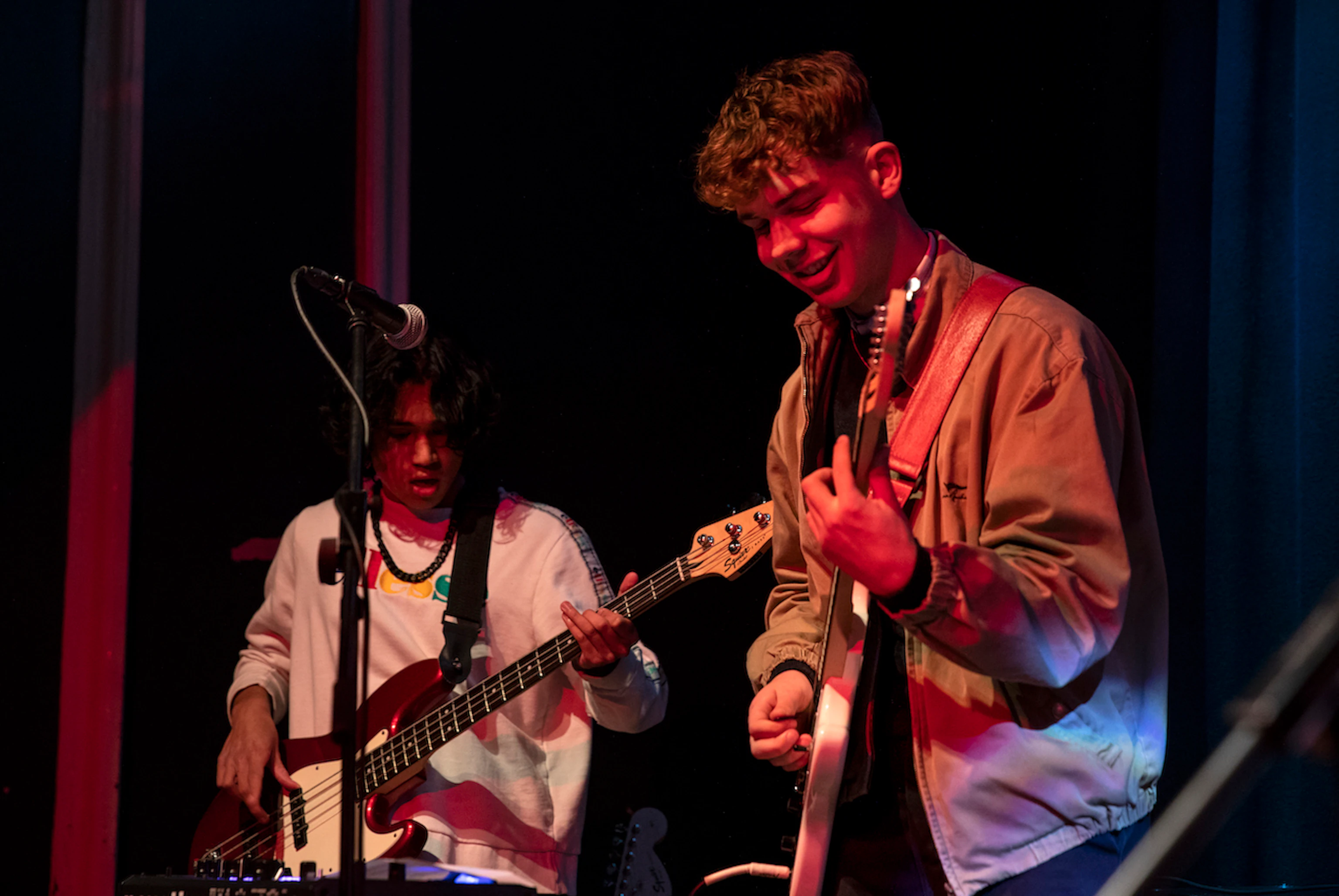 Two young musicians on stage playing guitar and smiling.