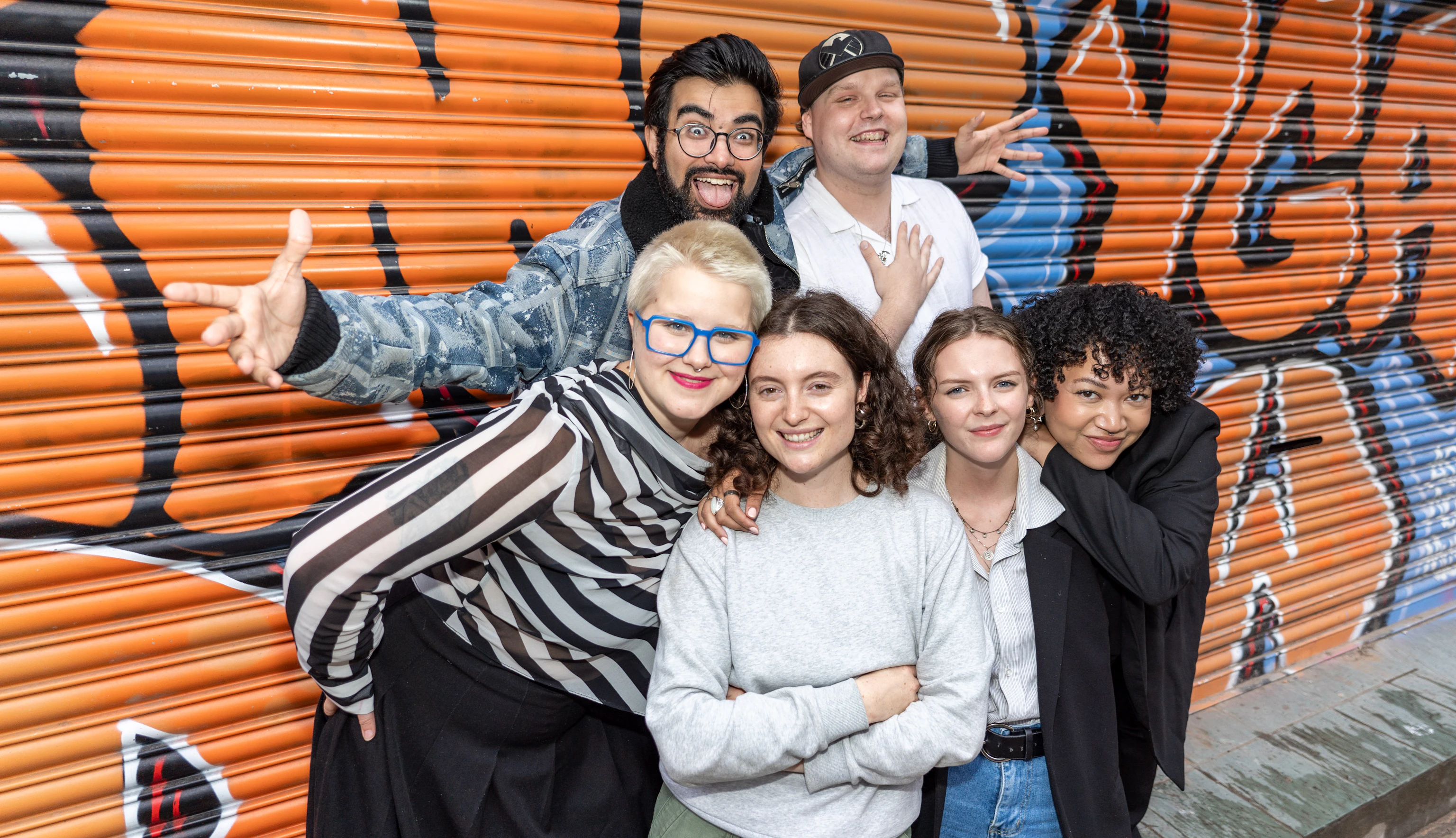 A group of young creatives posing together in front of orange graffiti.