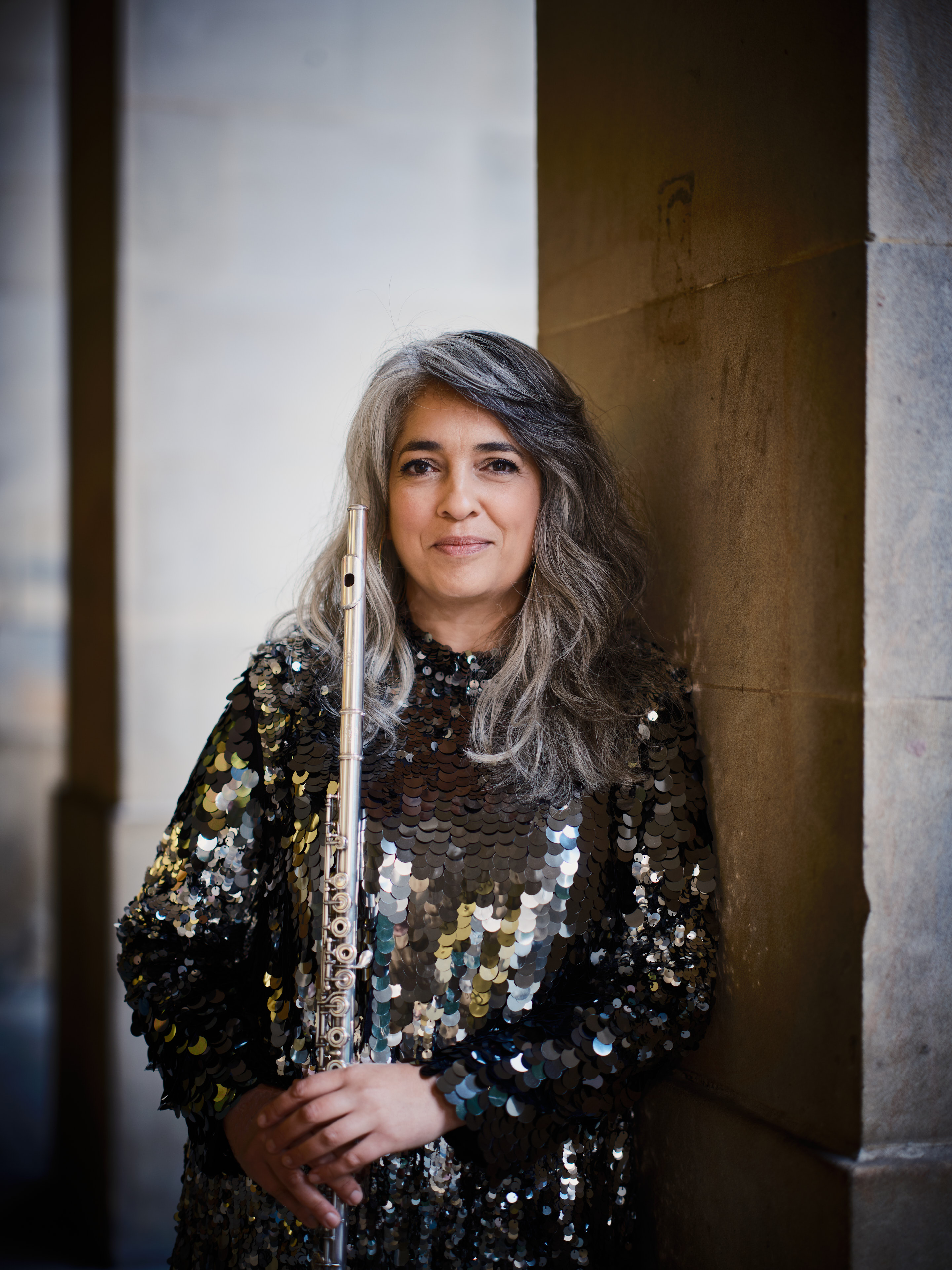 Amina Hussain leaning by a stone pillar holding a flute.