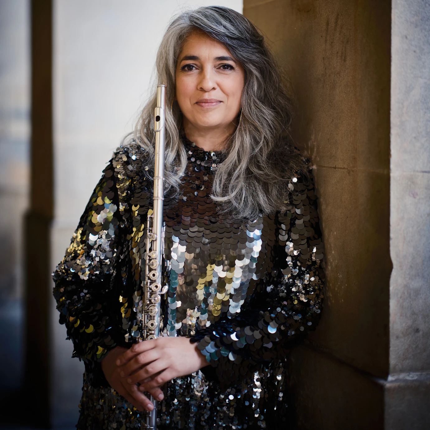 Amina Hussain leaning by a stone pillar holding a flute.