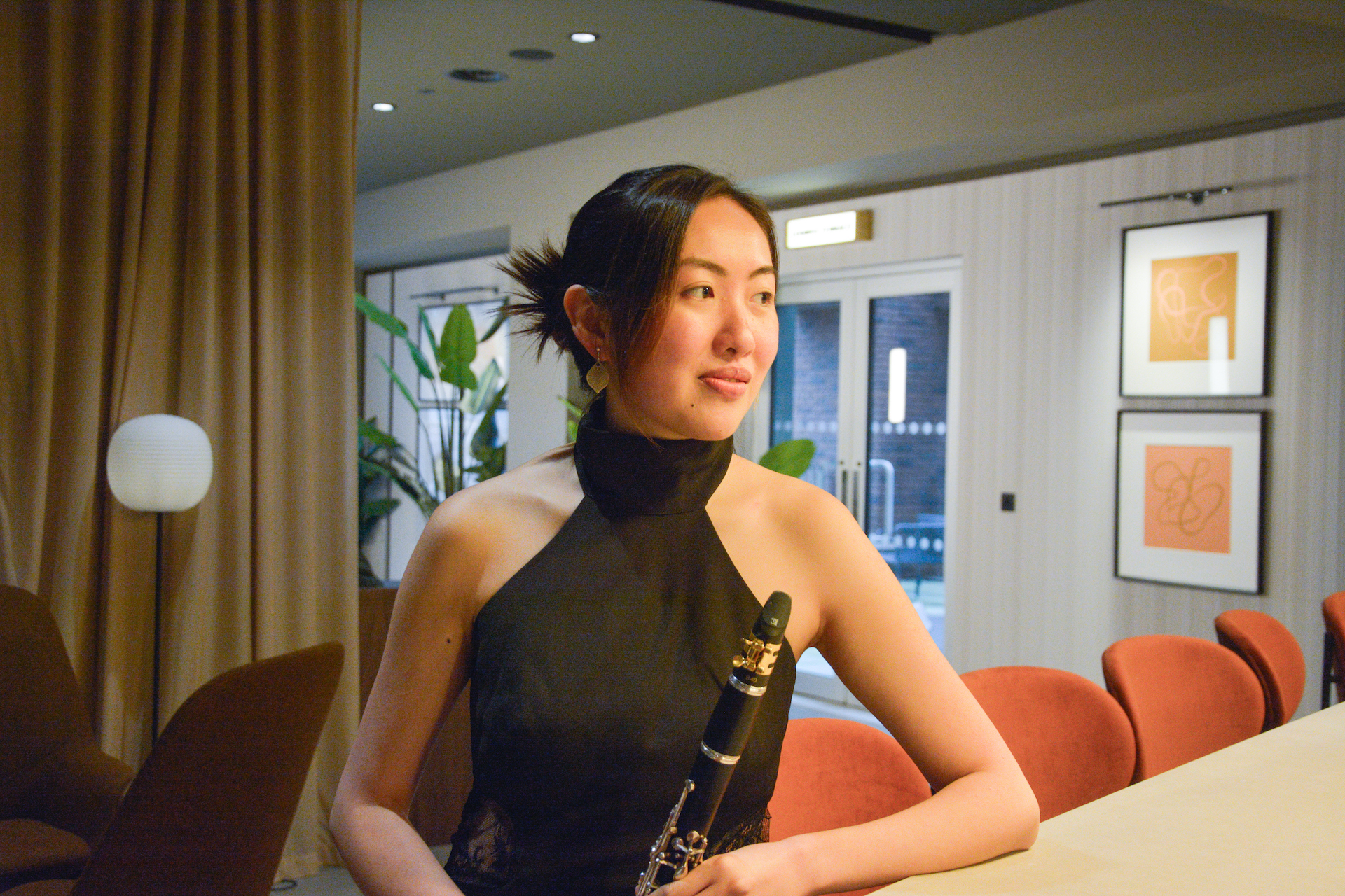 Johanna Leung sat by a desk, smiling, lit by a warm light and holding a clarinet.