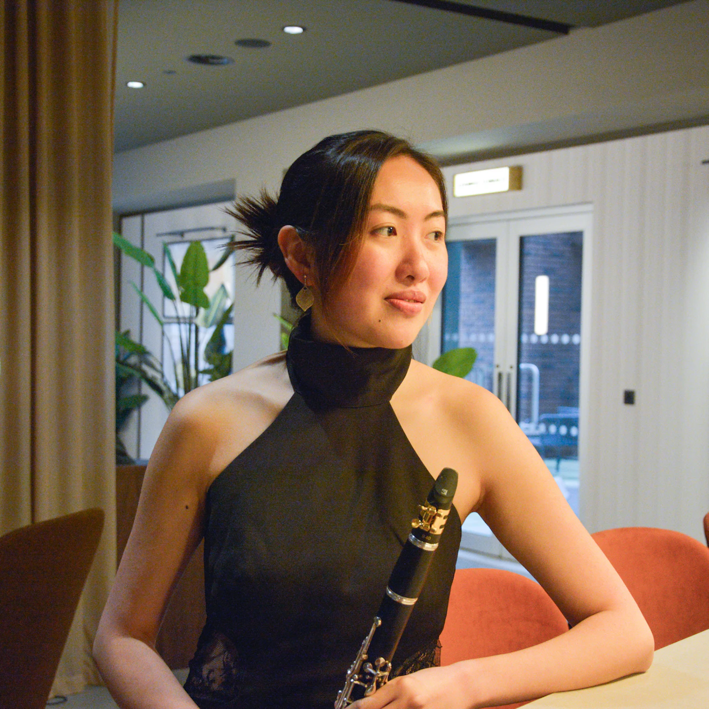 Johanna Leung sat by a desk, smiling, lit by a warm light and holding a clarinet.