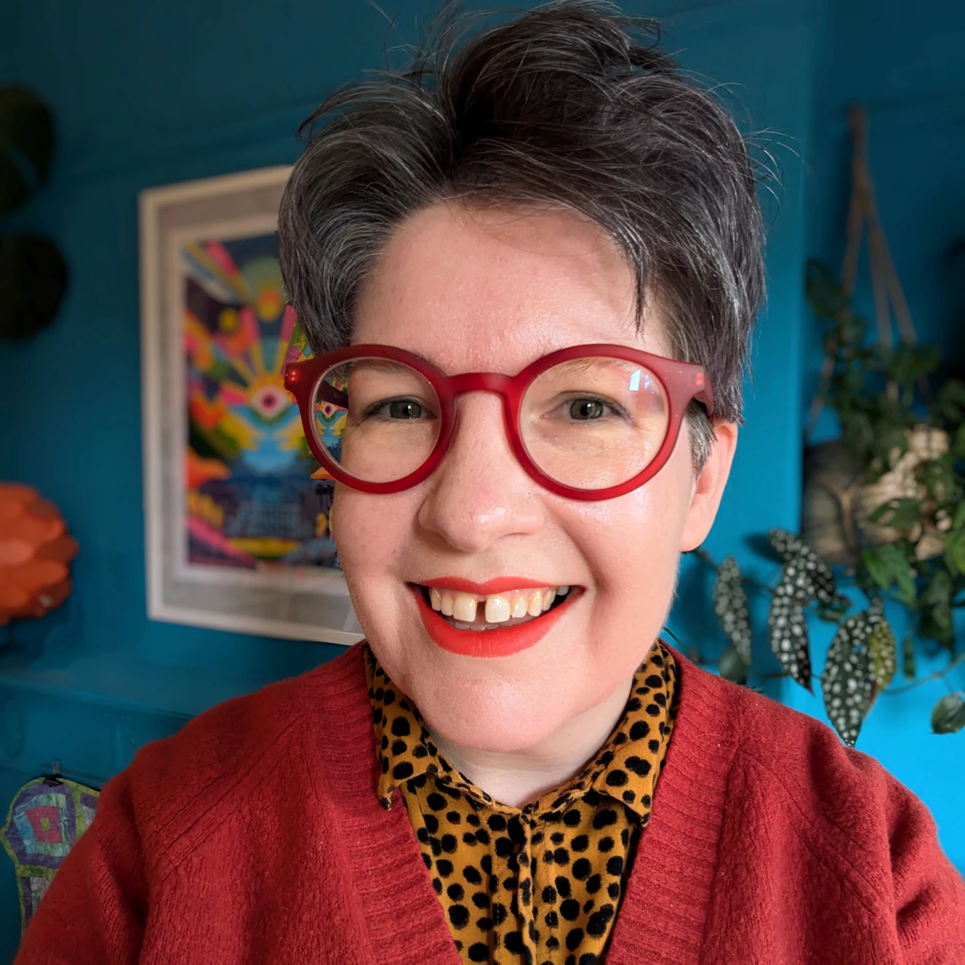 Laura Simms-Luddington smiling to camera in a homely setting with blue walls.