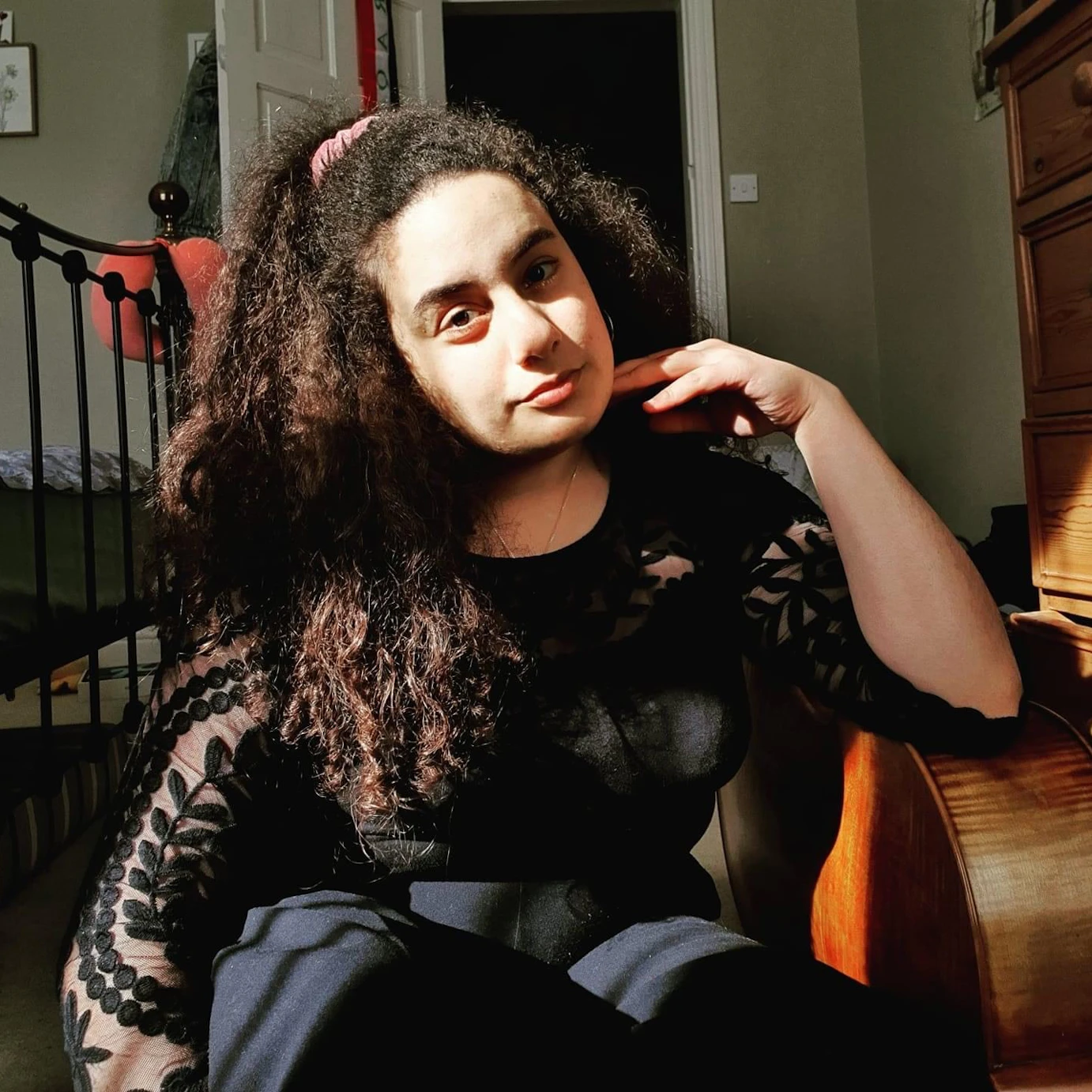 Reyan Murtadha crouched on the floor of a bedroom with one elbow leant on the side of a cello.