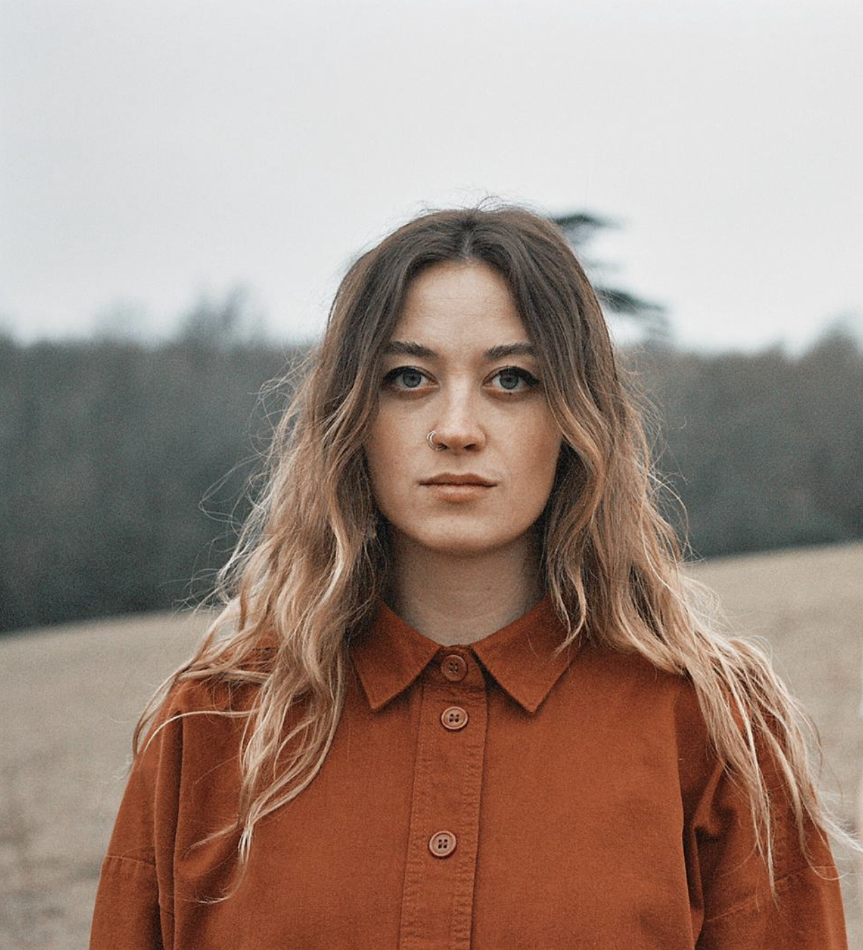 Amy Illingworth looking to camera stood in a field with trees in the horizon on an overcast day.