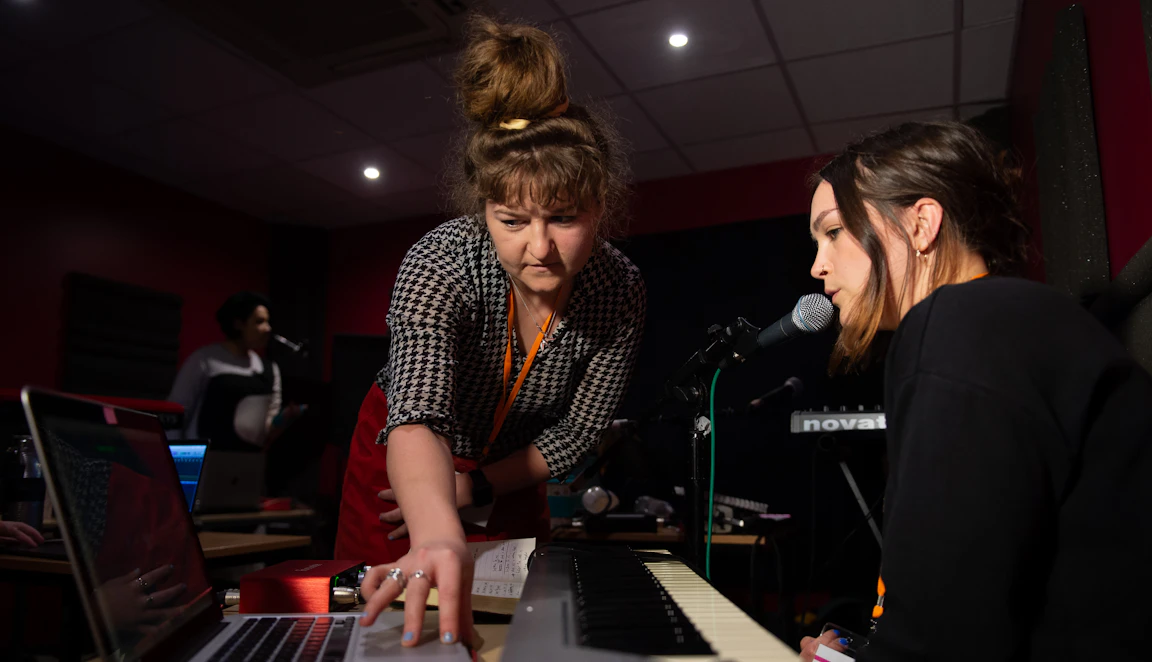Holly leans over to a laptop to support a participant who is singing into a microphone.