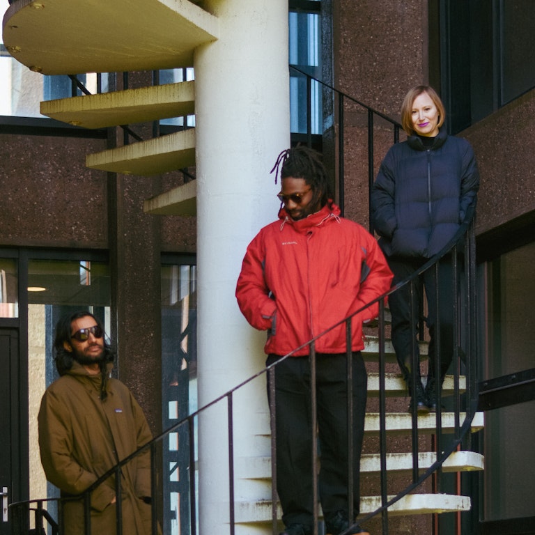 Balraj, Tunde and Kamila stand together on a spiral staircase. 