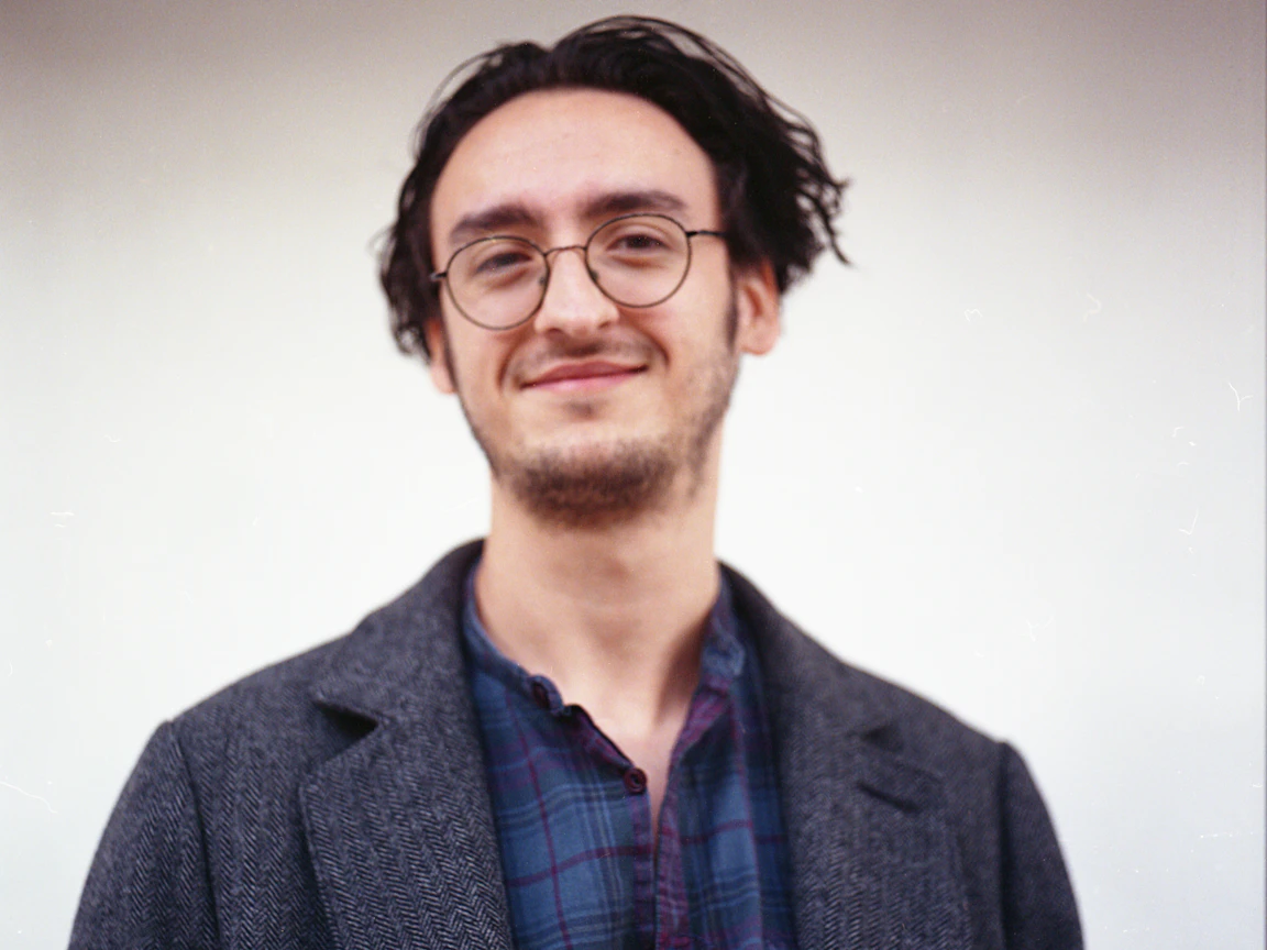 Joe smiles at the camera and is wearing a grey coat.