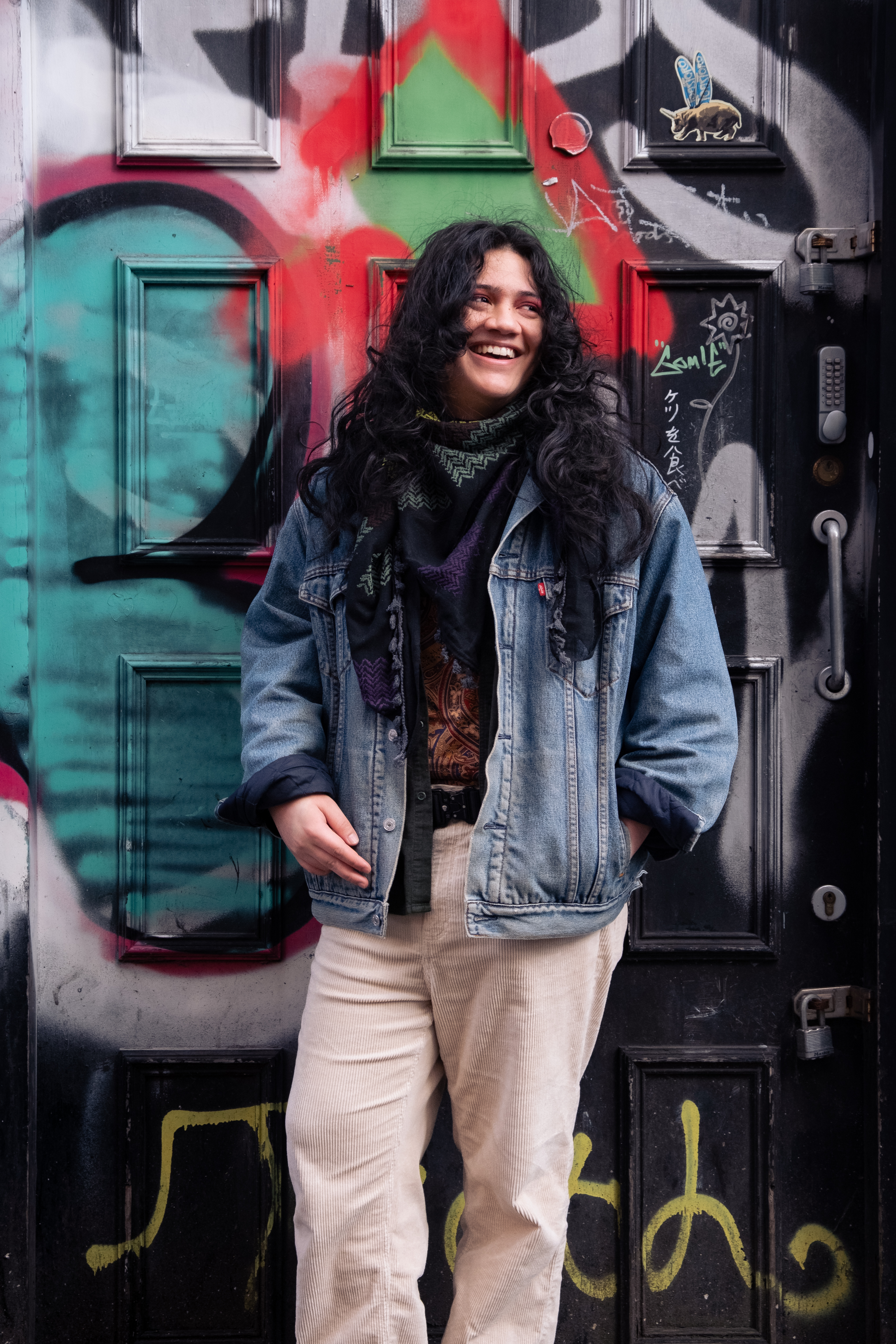 yeguachita smiling stood against a wall with lots of graffiti.
