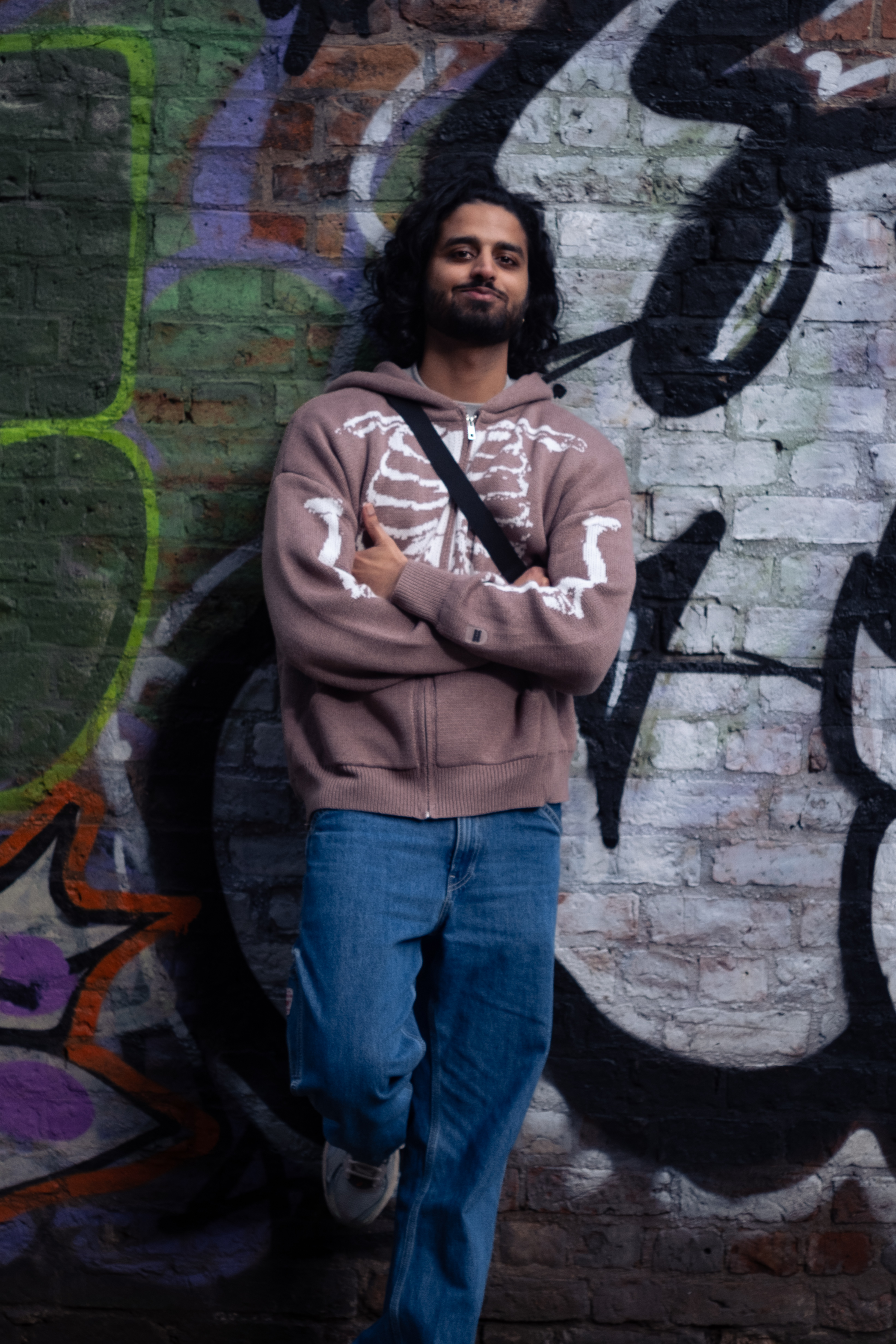 Scytale leaning against a wall with lots of graffiti.