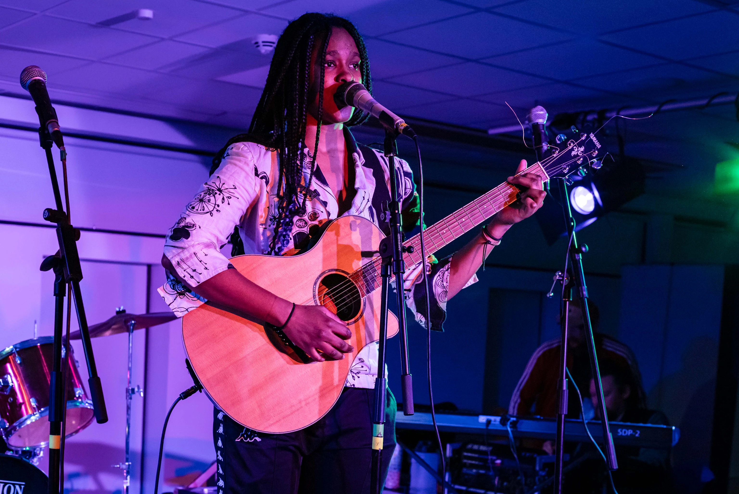 A young musician playing acoustic guitar and singing on stage.