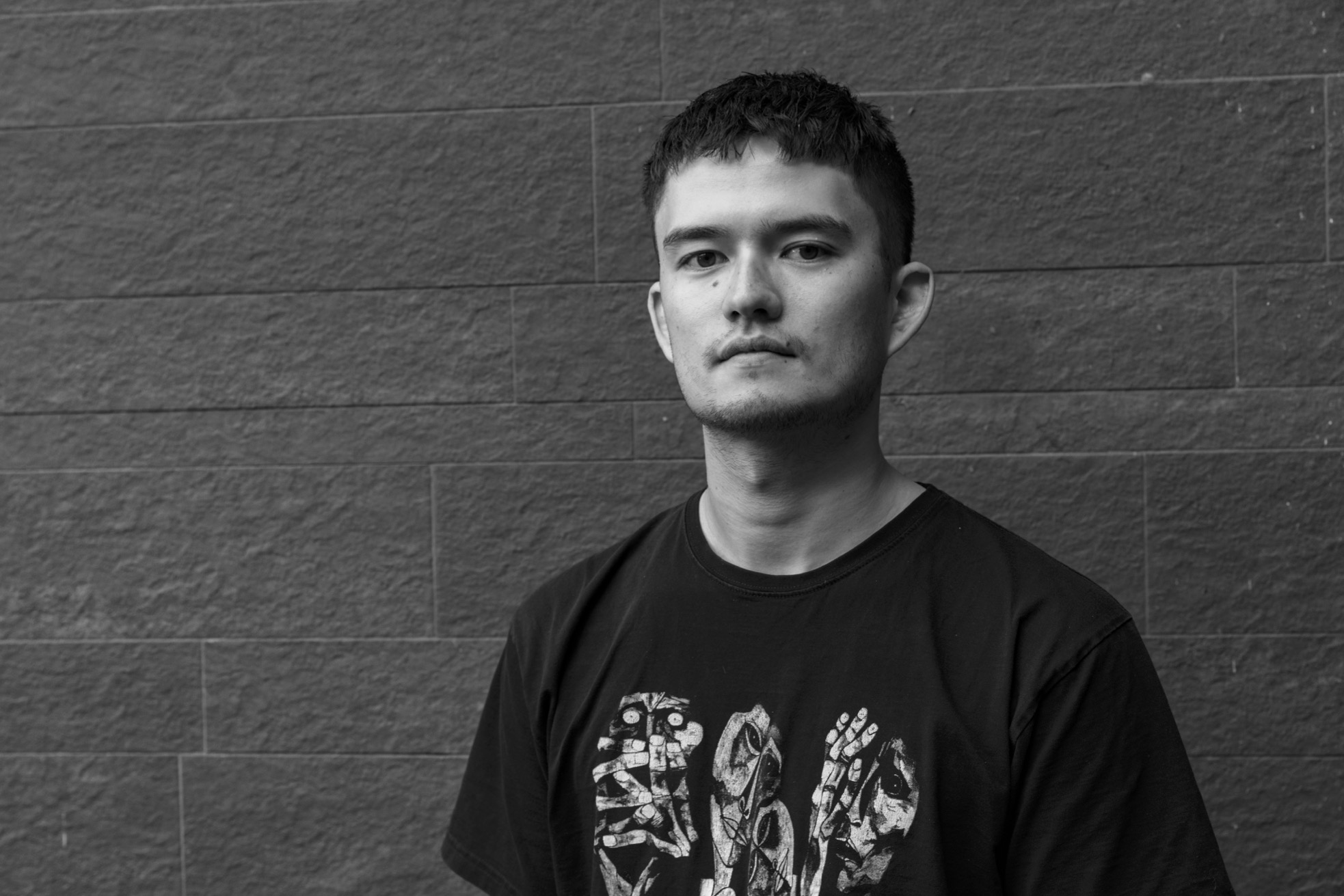 Kai Chareunsy looking to camera on a brick background. The photo is black and white.
