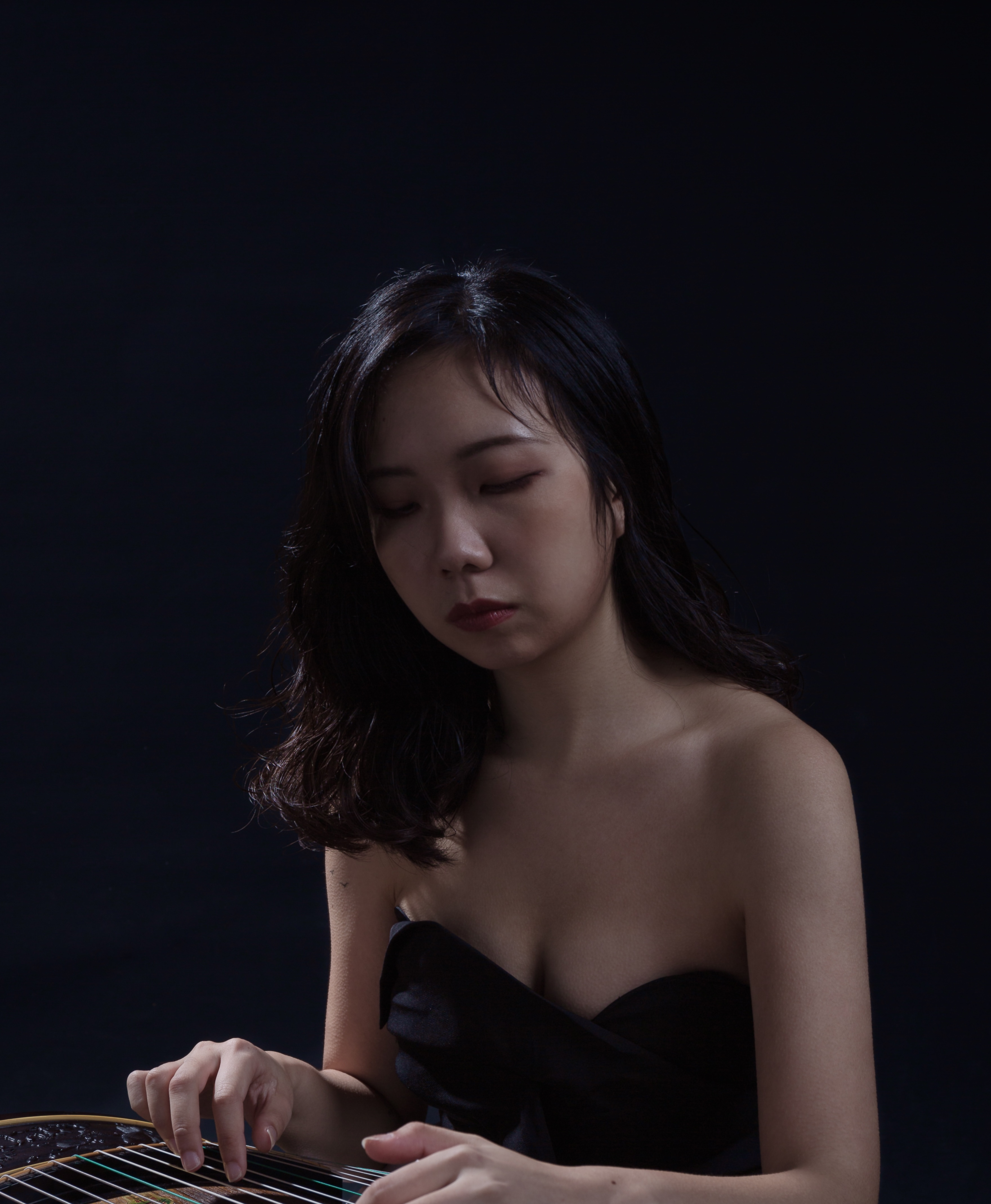 Katherine Lee in a dark room playing a string instrument.