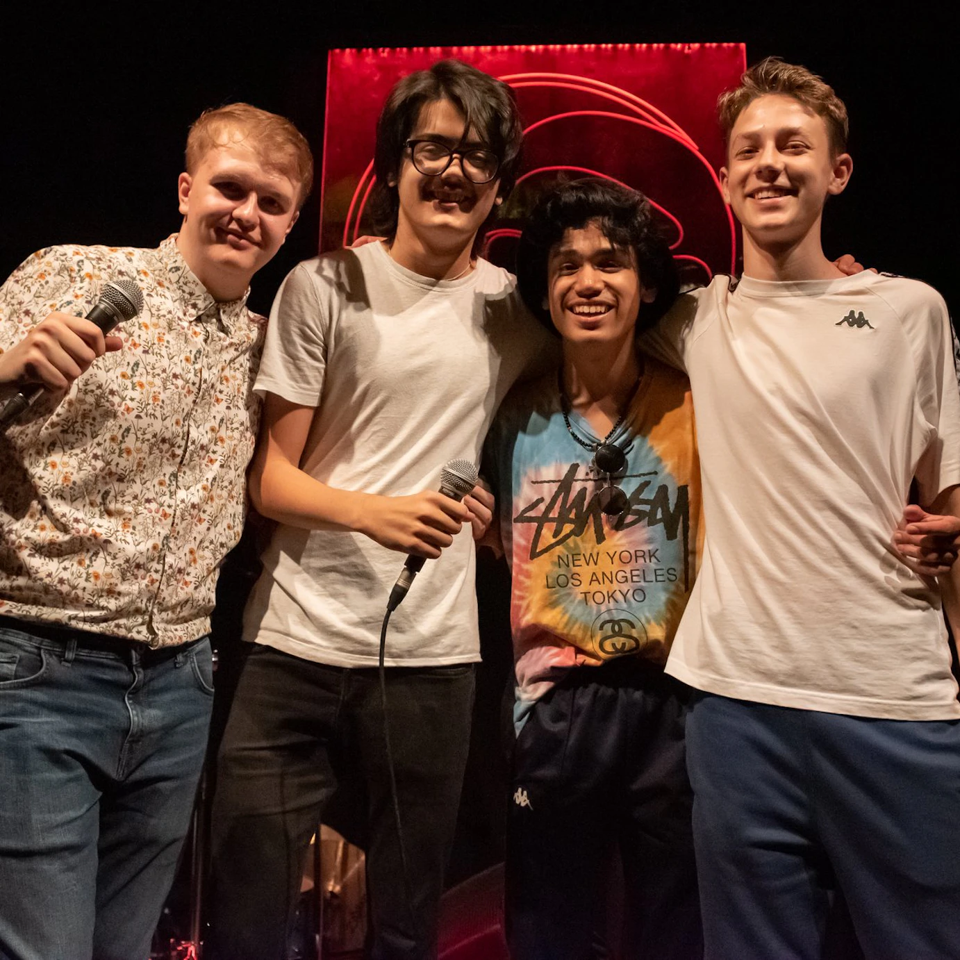 Tom and 3 other young musicians arms linked and smiling to camera.