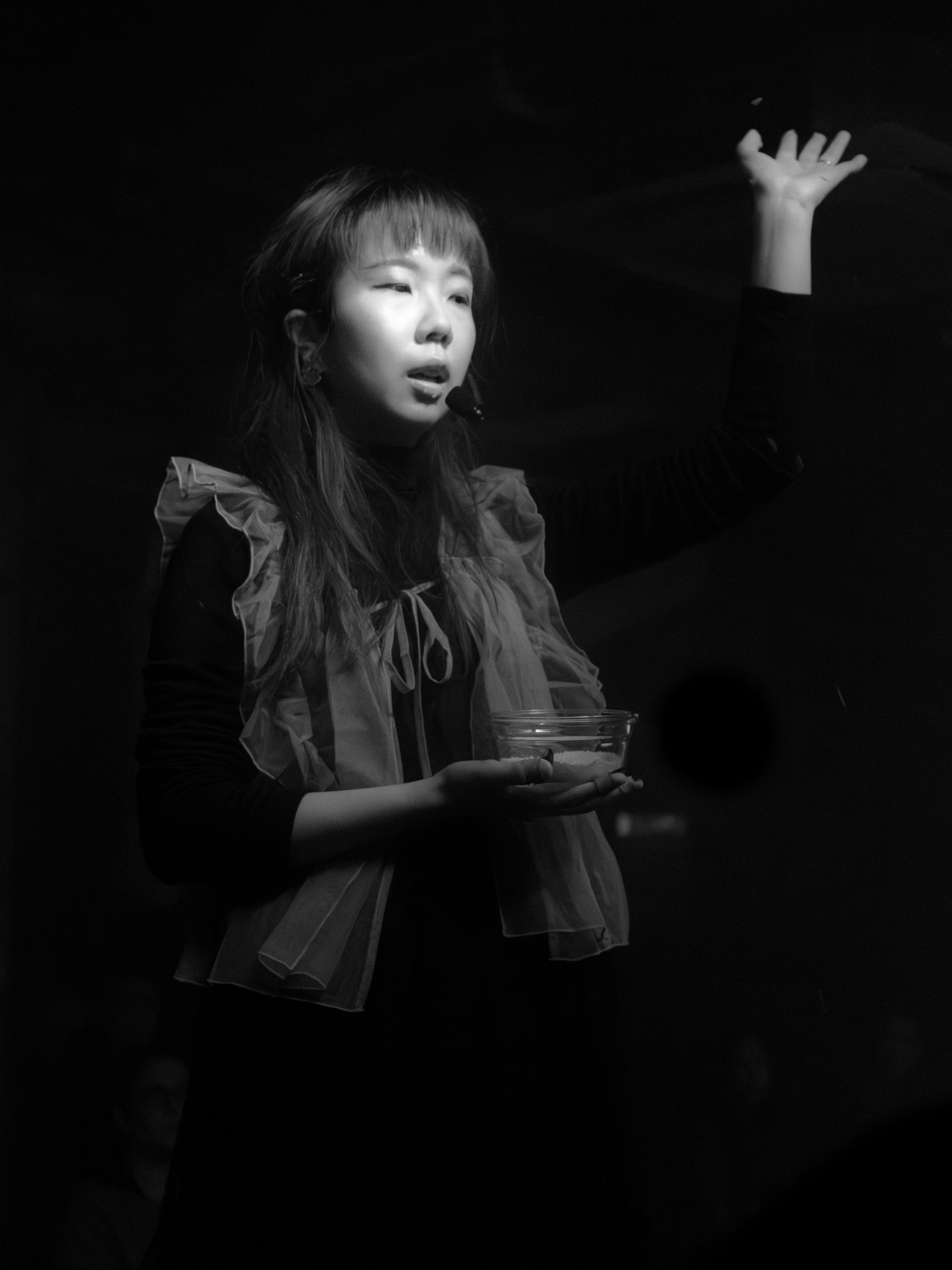 Katherine providing spoken word and holding a bowl of rice with one hand in the air.