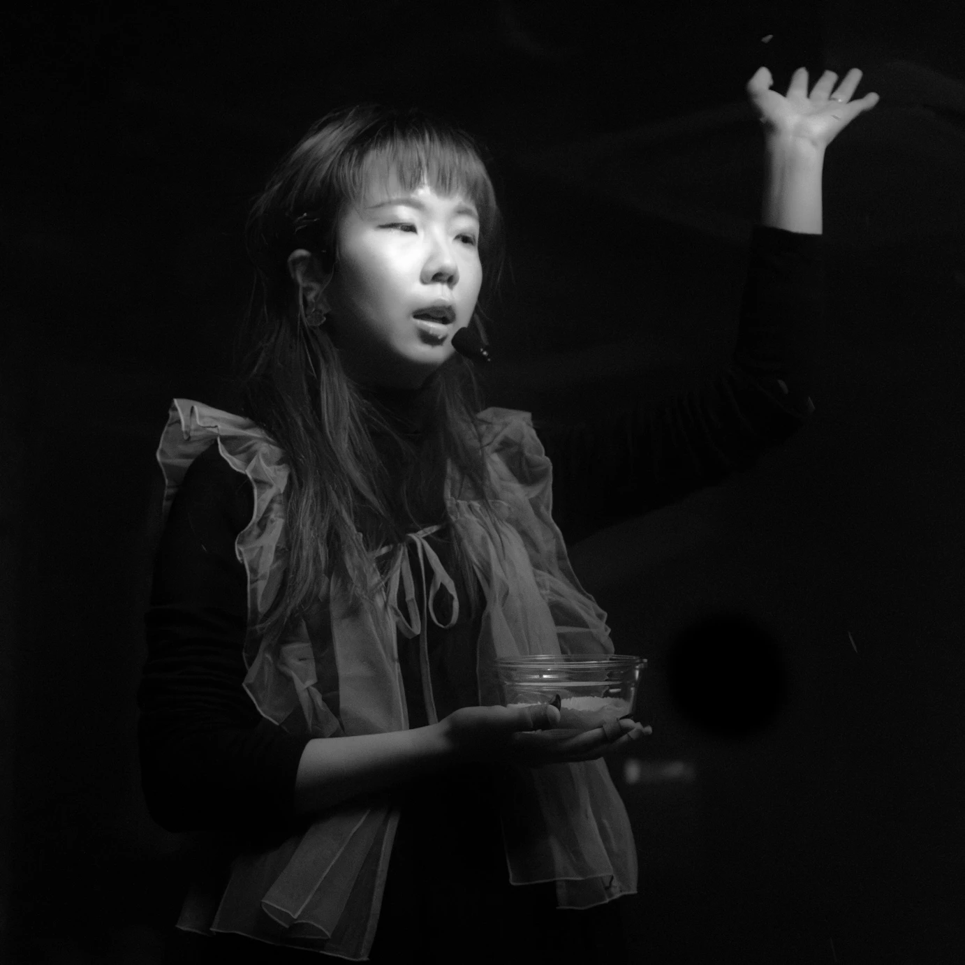 Katherine providing spoken word and holding a bowl of rice with one hand in the air.