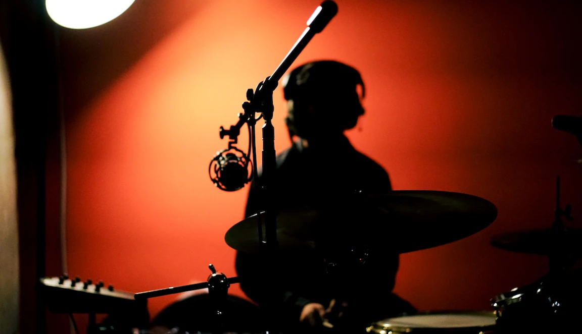 A silhouette of a young musician in VoltaLab with headphones on whilst sat by a drum set.