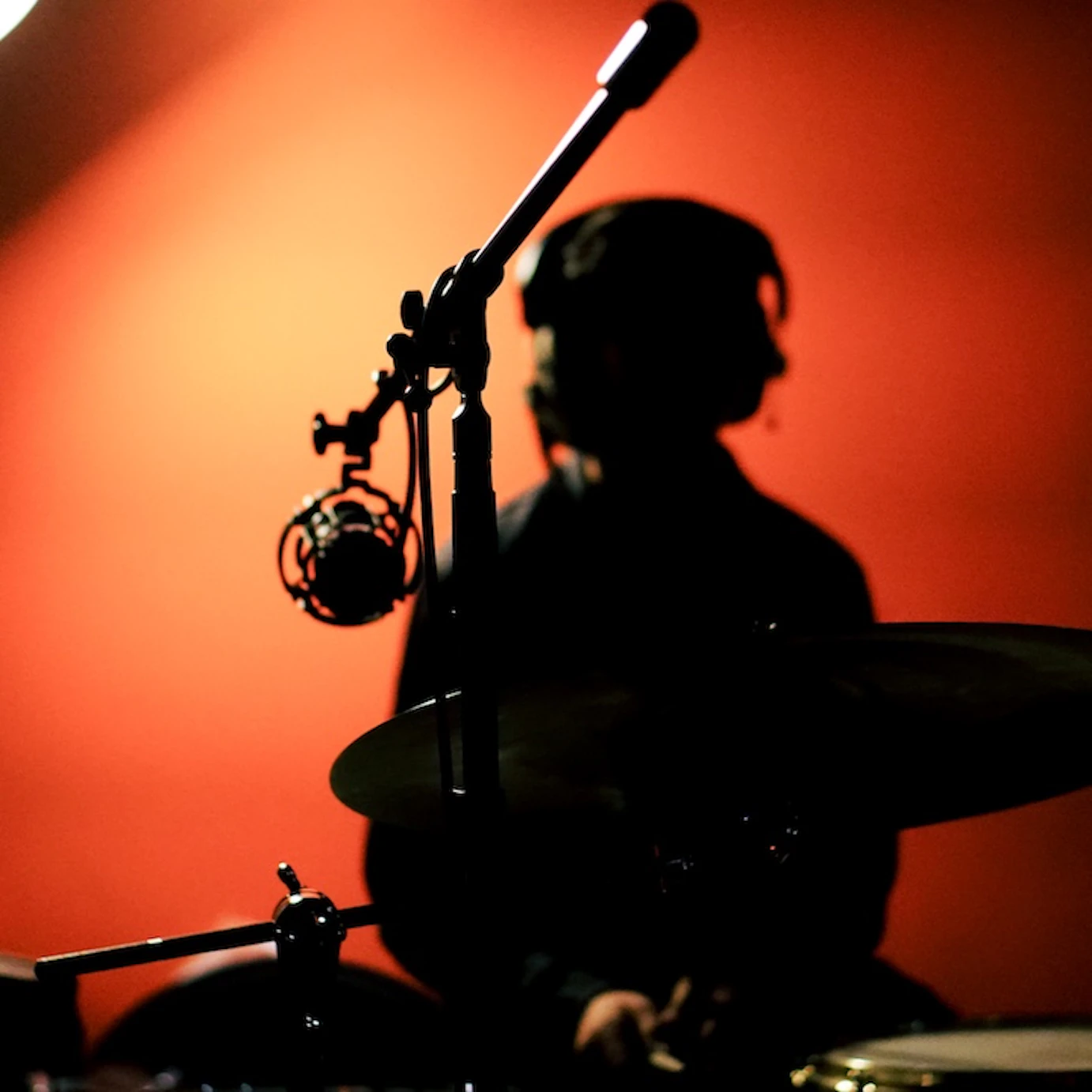 A silhouette of a young musician in VoltaLab with headphones on whilst sat by a drum set.