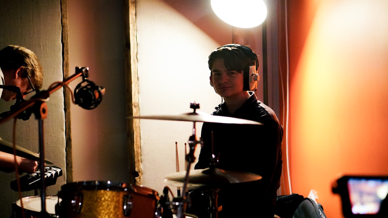 A young musician in VoltaLab with headphones on whilst sat by a drum set.