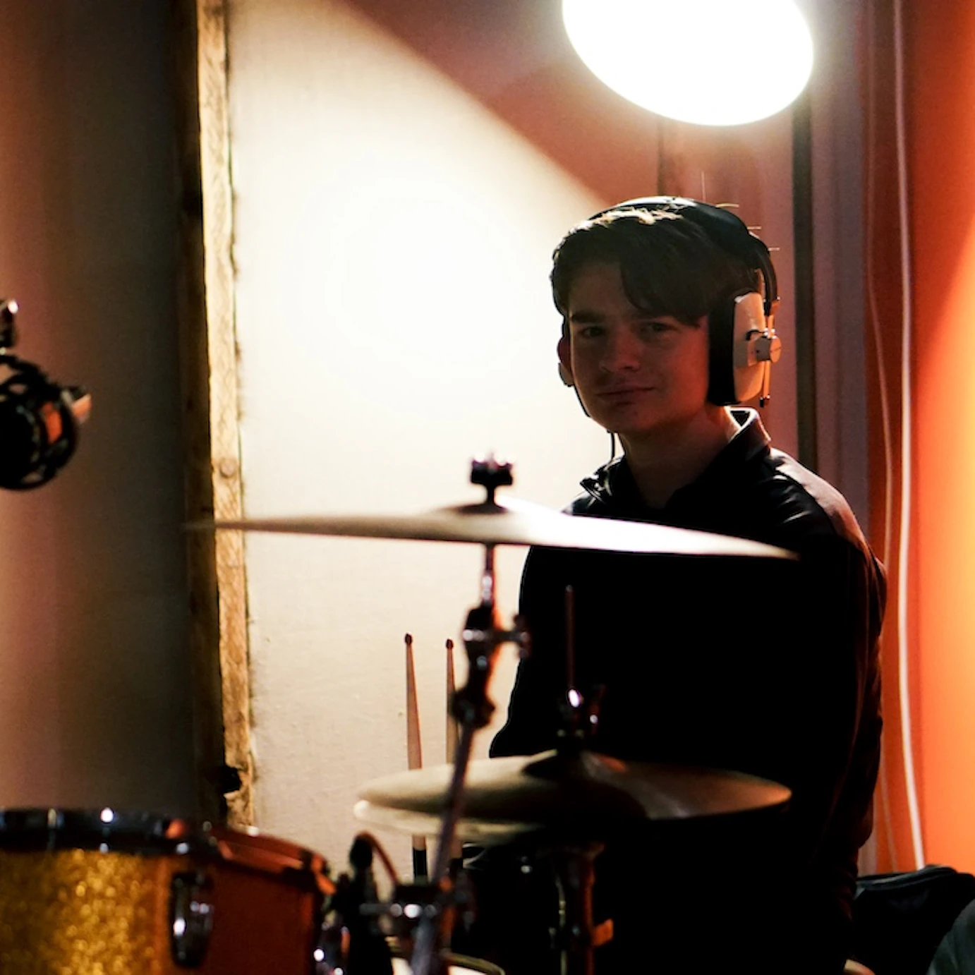 A young musician in VoltaLab with headphones on whilst sat by a drum set.