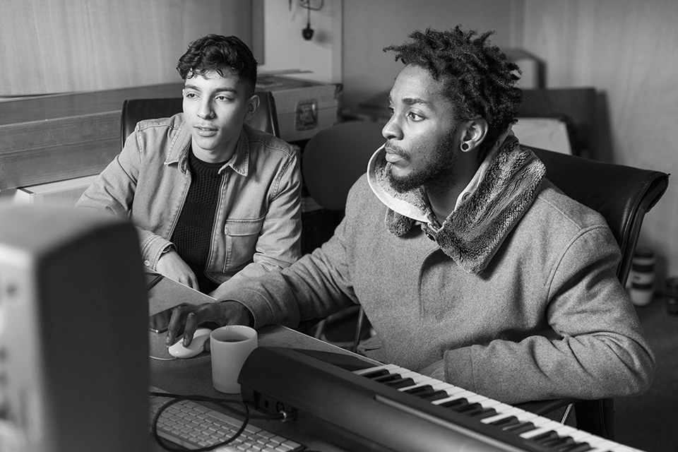 A young musician sat by a facilitator by a desk watching the screen.