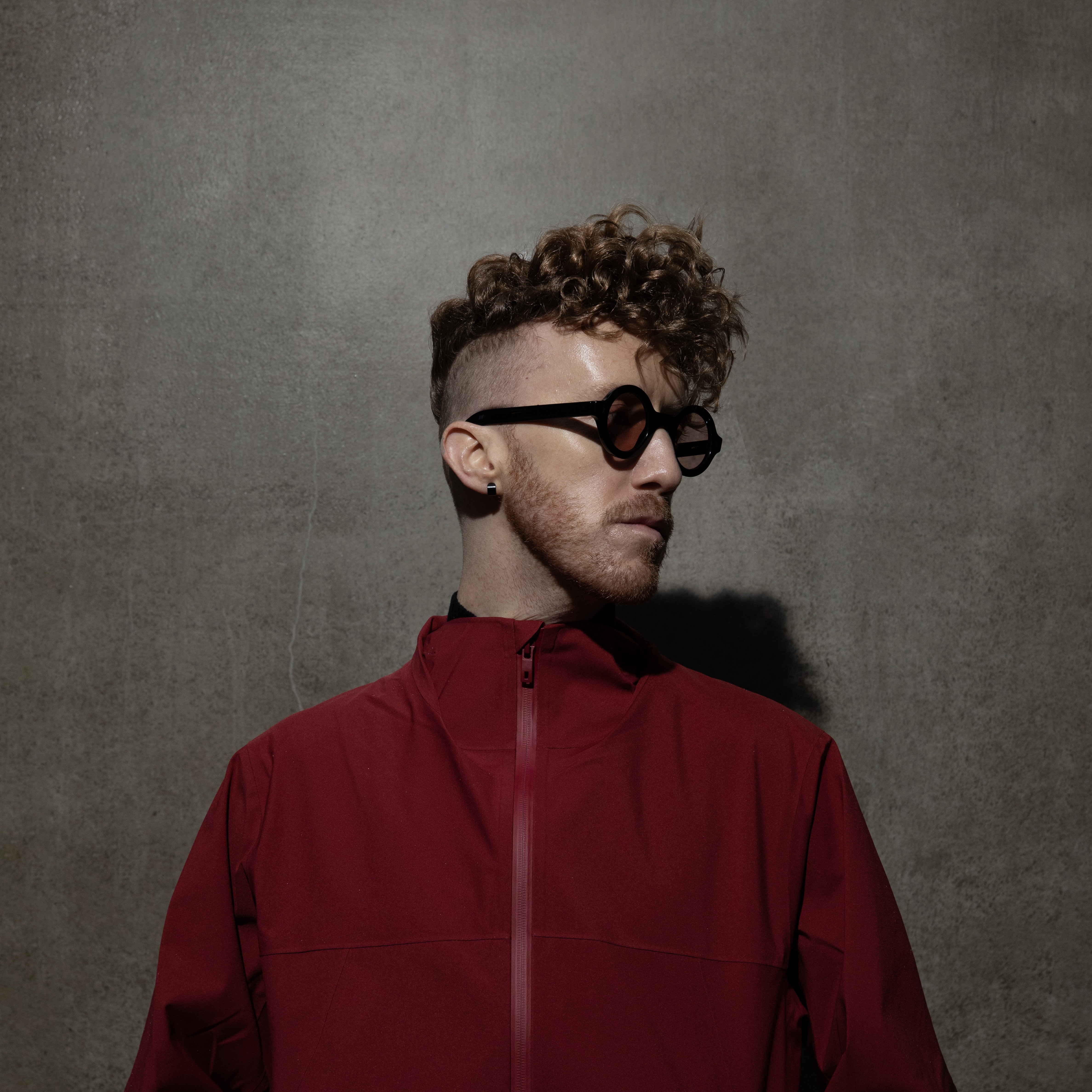Daley with circular sunglasses in front of a grey wall.
