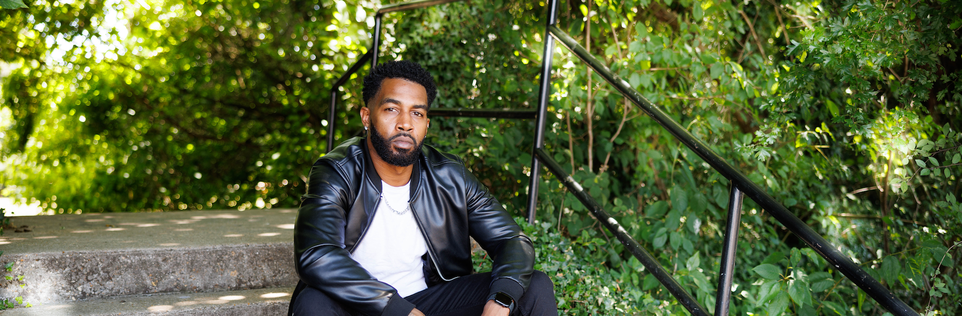 Didier Atine sat on some steps outdoors surrounded by trees.