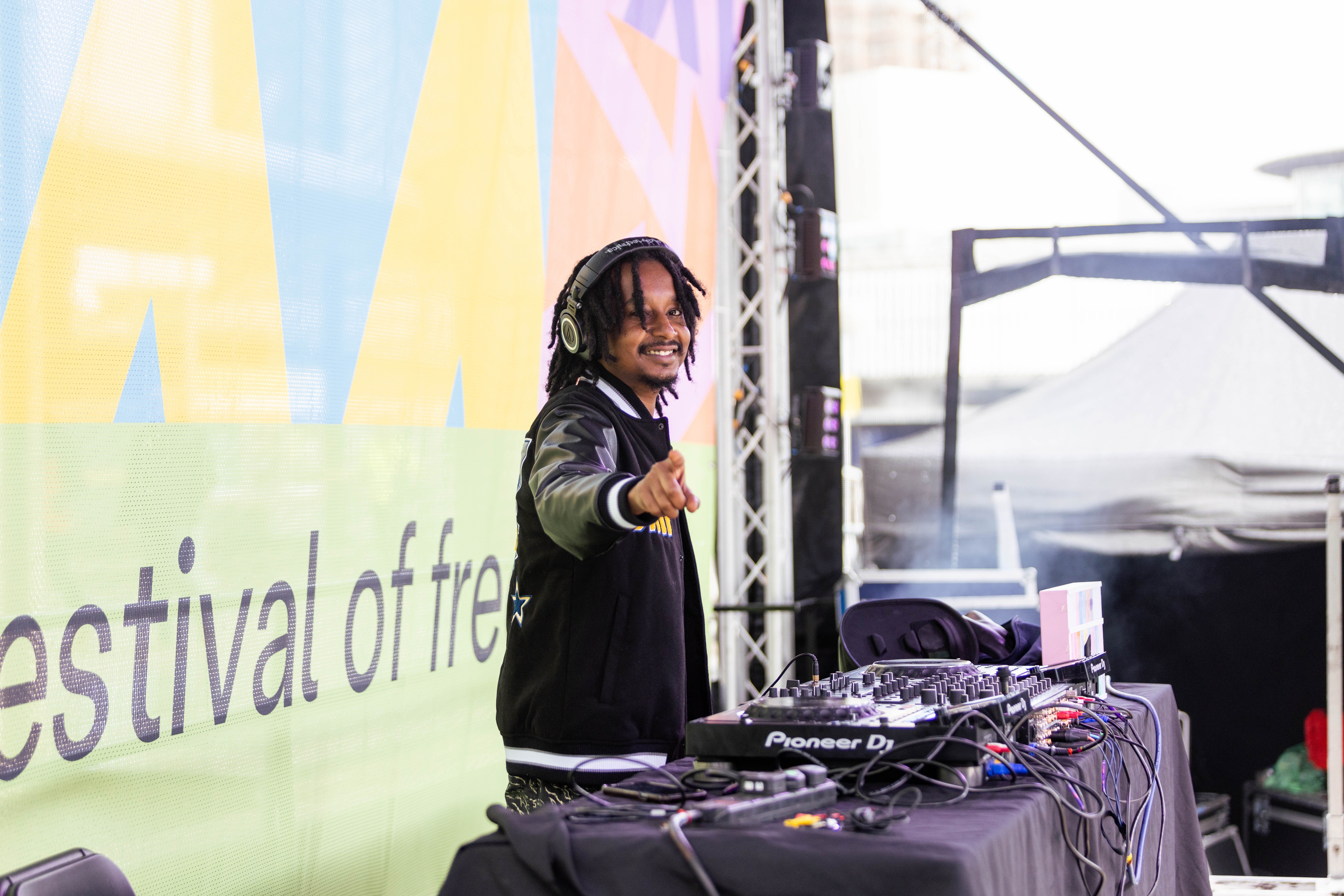 DJ Roesh smiling and pointing to camera whilst DJing on stage.