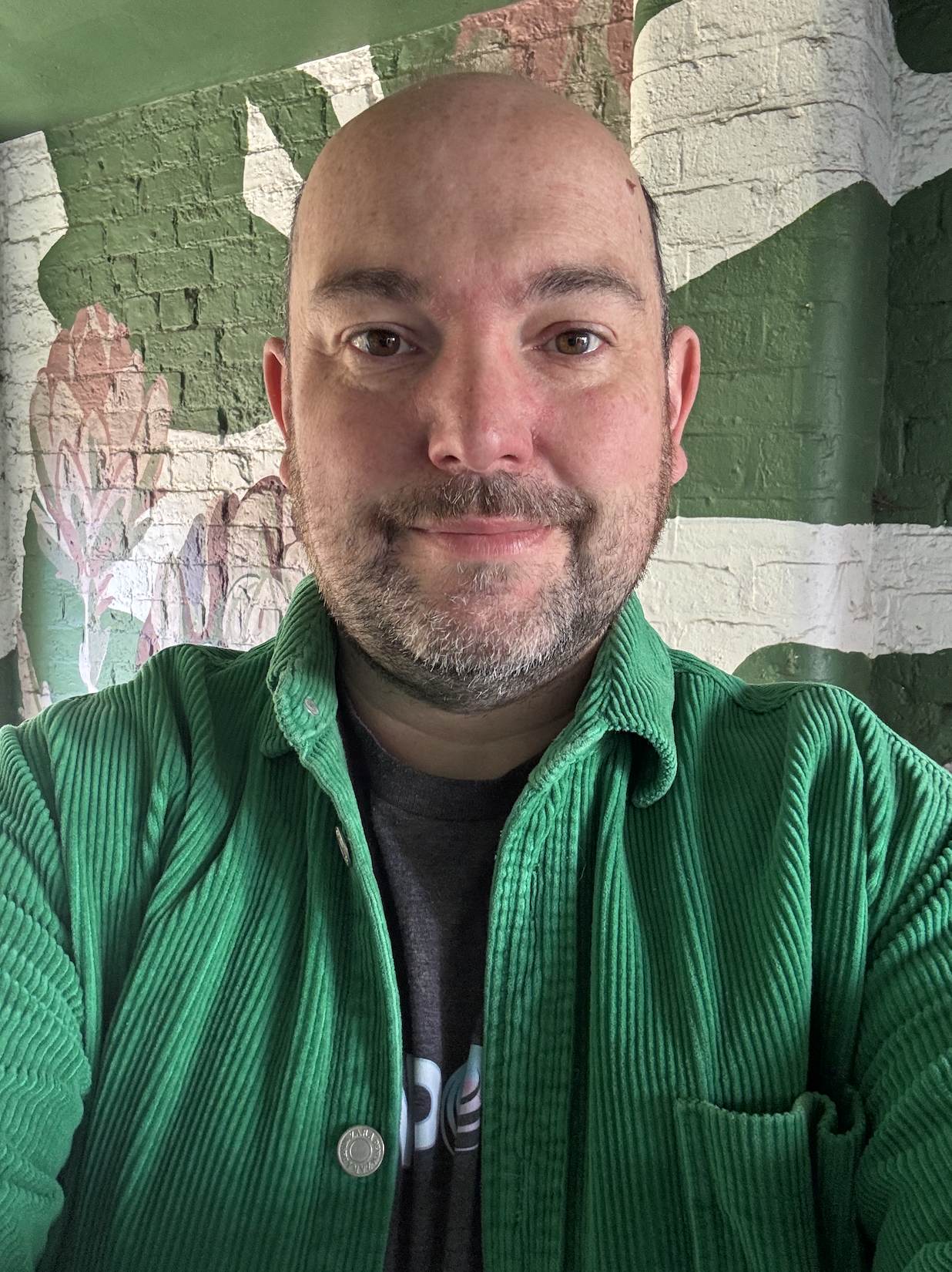 Phil Charnock looking to camera in front of a painted wall.