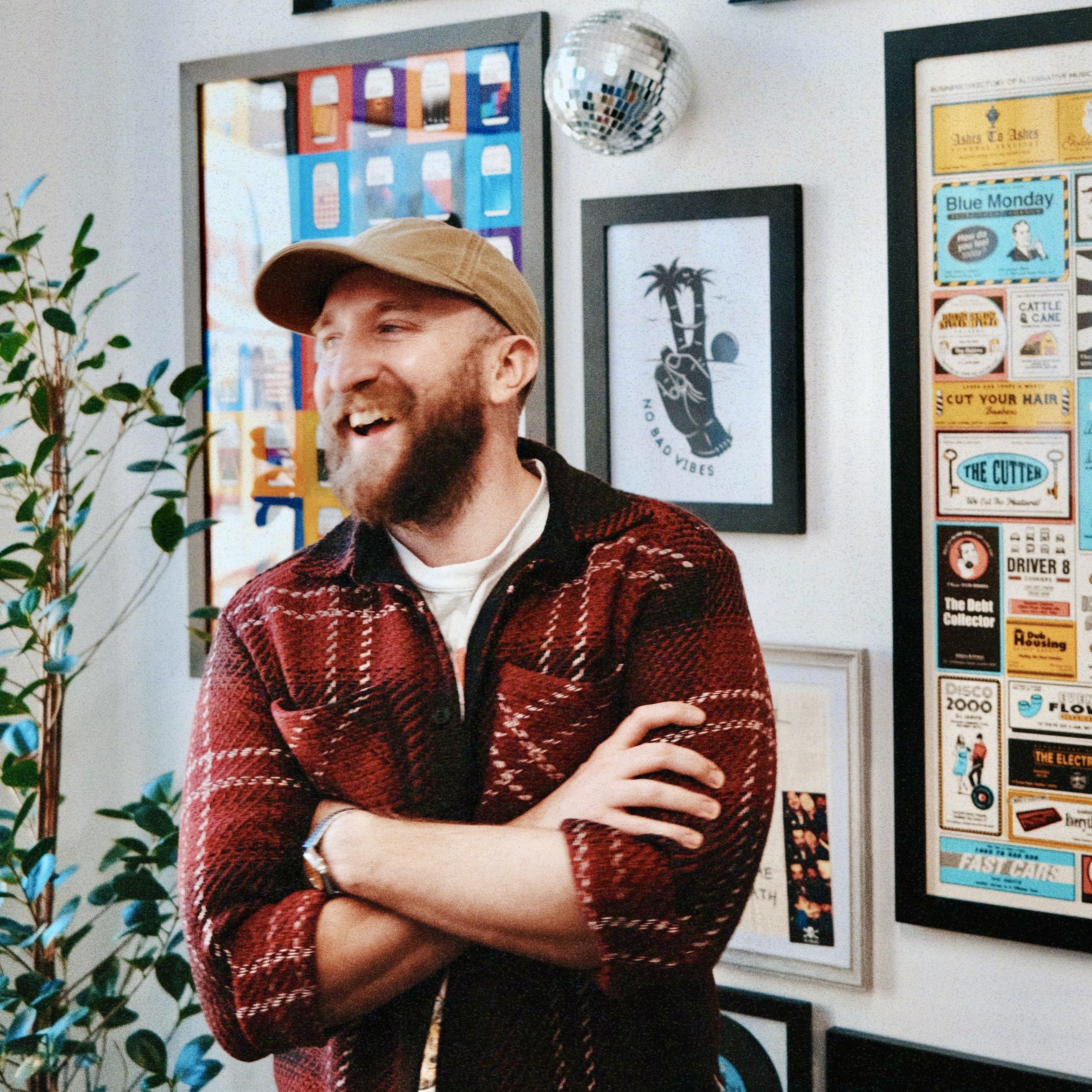 Simon Pursehouse smiling in a room against a wall layered with different artworks in frames.