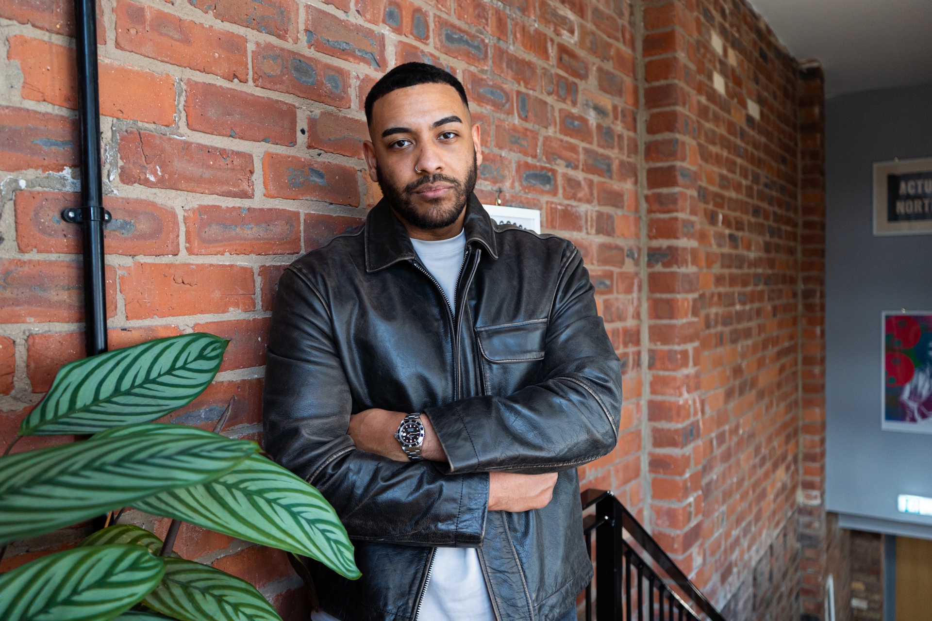 Josh Daniel leaning against a brick wall with arms folded.