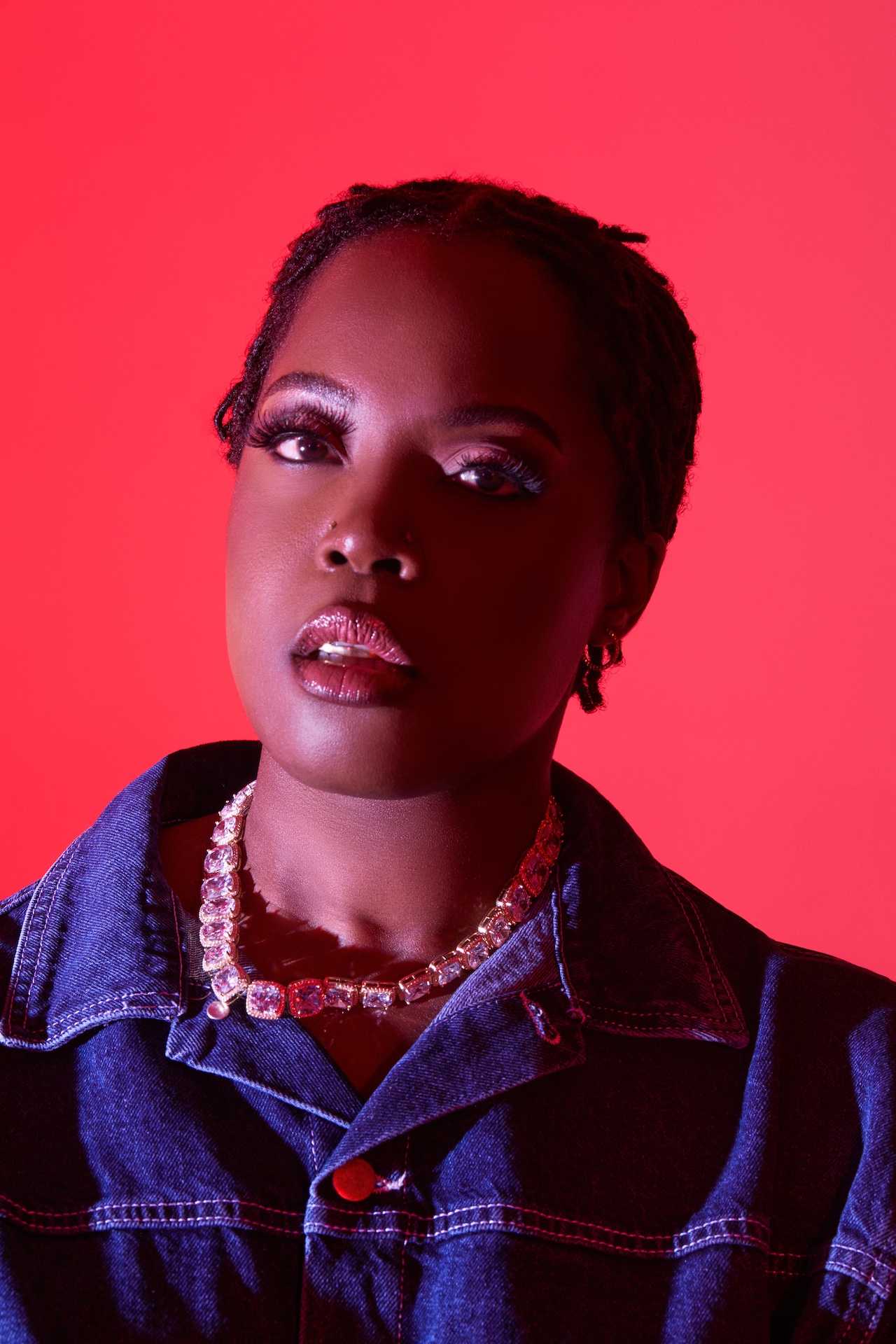 Karen Nyame KG looking to camera on a light red background.