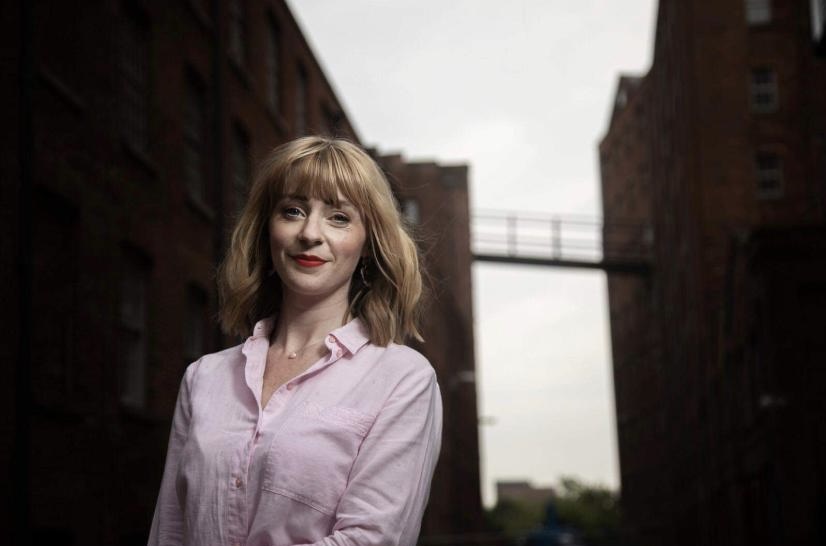 Rachel Waters outside surrounded by buildings smiling to camera.