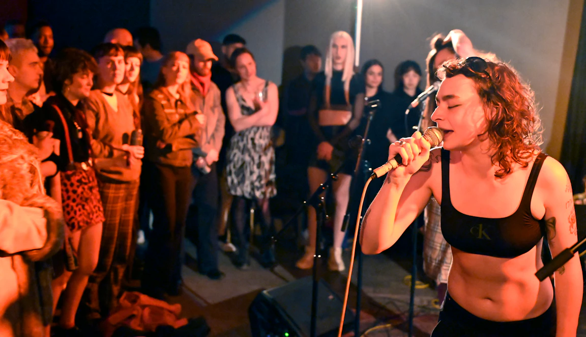 A residency artists singing into a mic in front of a crowd.