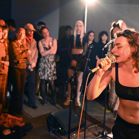A residency artists singing into a mic in front of a crowd.