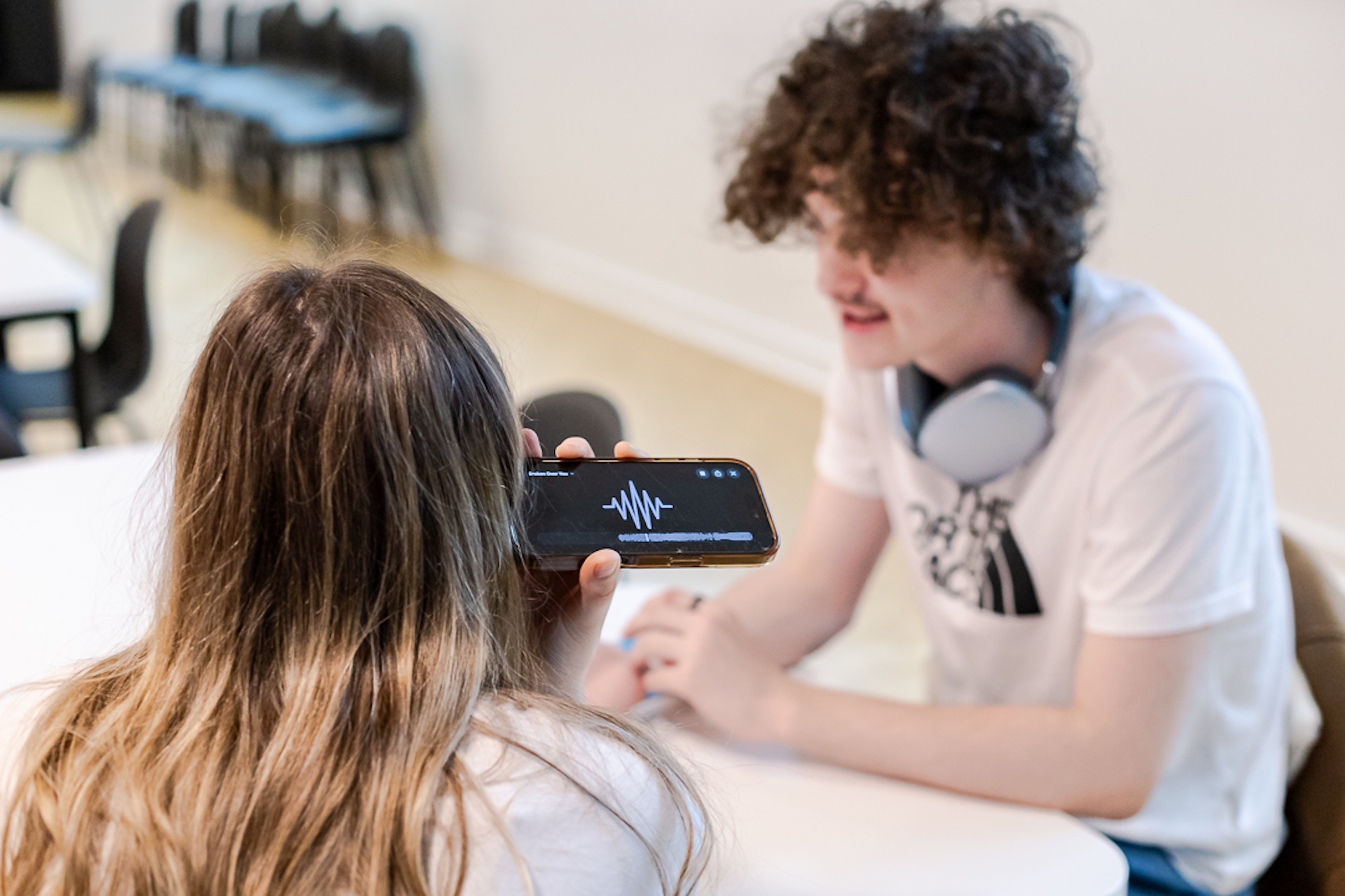 A young musician sat chatting with an industry professional who is listening to one of their tunes on a phone.