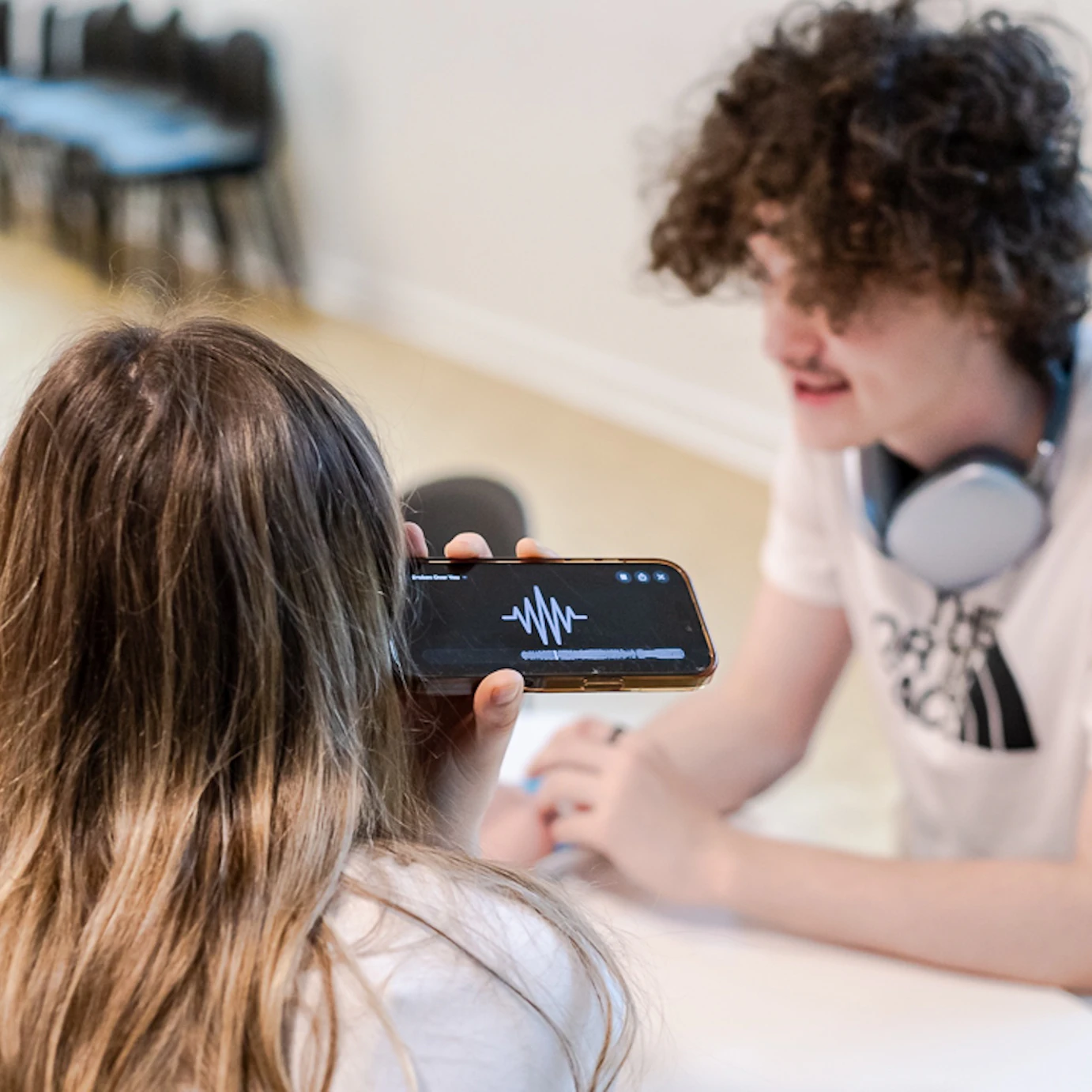 A young musician sat chatting with an industry professional who is listening to one of their tunes on a phone.