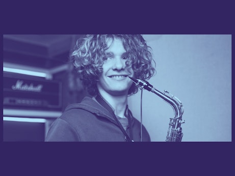 A young musician smiling and holding a saxophone close to their face. The photo is tinted light blue on a navy blue background.