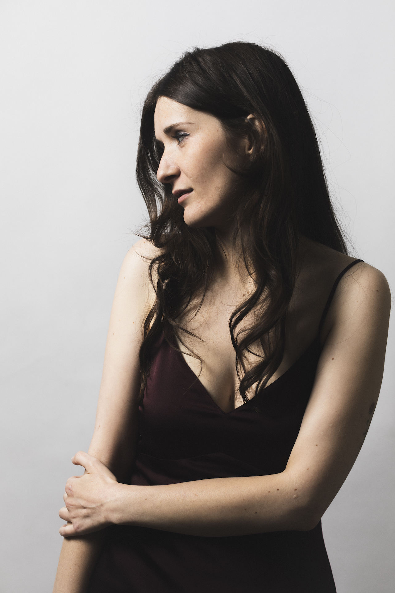 Megan Steinberg wearing a dark brown dress. She is holding her right arm with her left hand and looking off to her right.