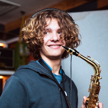 A young musician smiling and holding a saxophone close to their face.