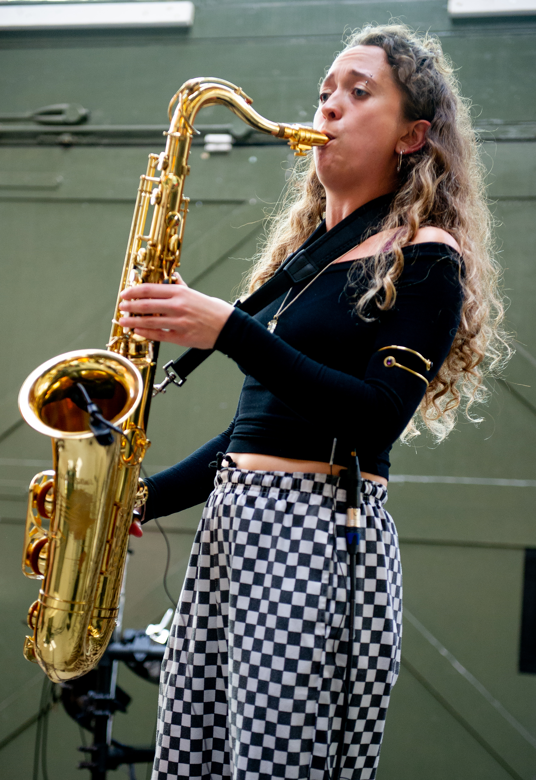Emily Kiely playing saxophone dressed in a black top and white and black checkered pants.