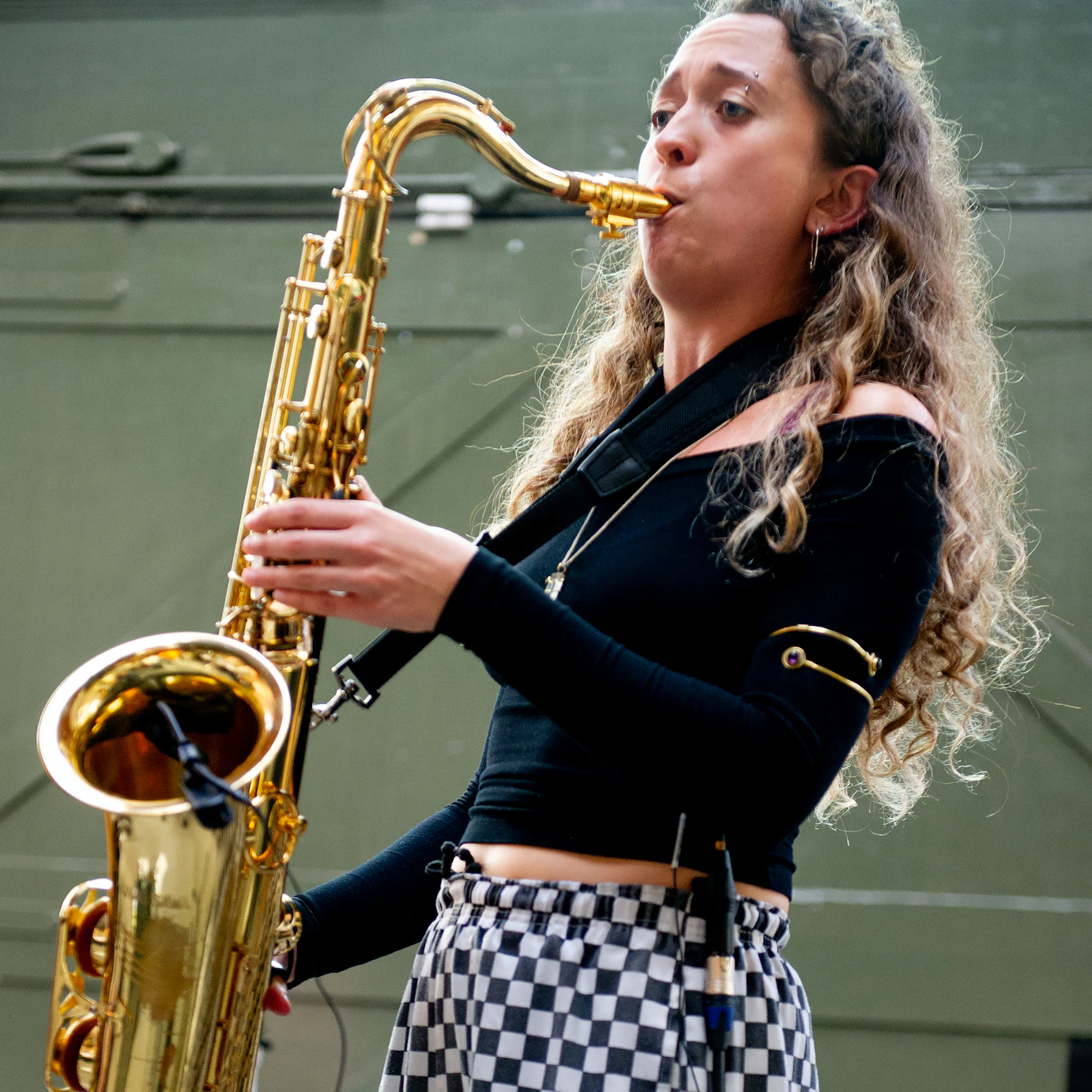 Emily Kiely playing saxophone dressed in a black top and white and black checkered pants.