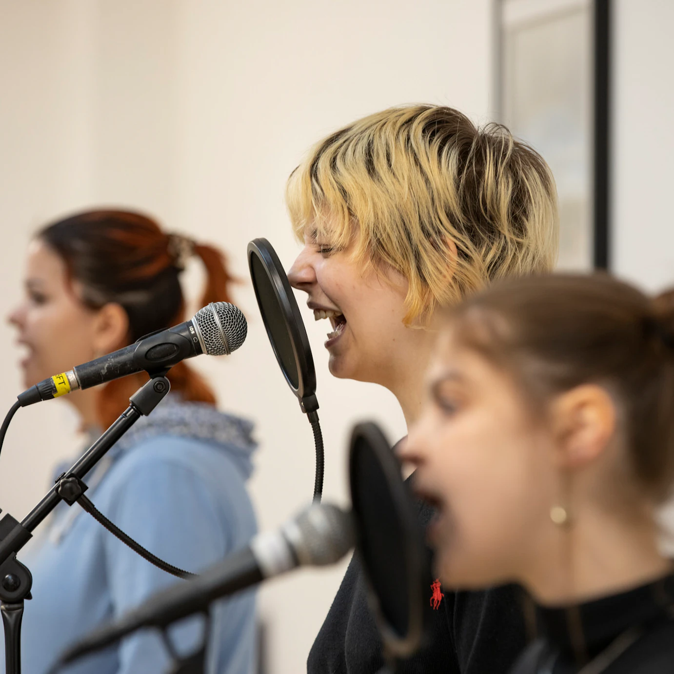 Three participants singing into microphones during rehearsals.