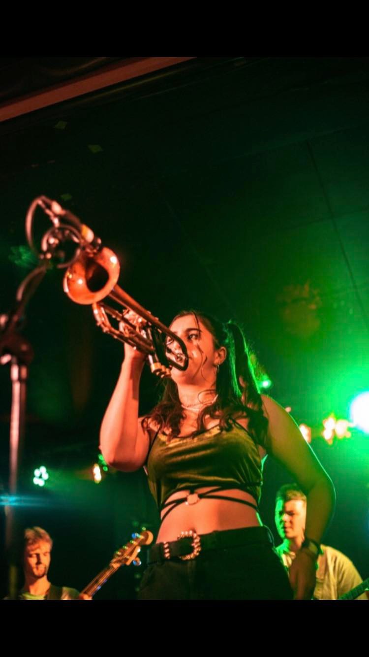 Fee on stage blowing into a trumpet.
