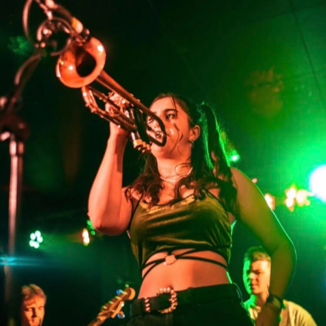 Fee on stage blowing into a trumpet.