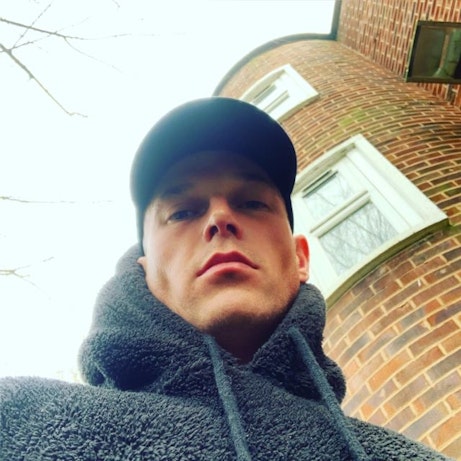 Danny Misell in front of a building looking into the camera, wearing a cap and a fluffy hoodie.