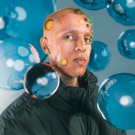 is33n is covered in digitally created bubbles of yellow and green, and orange lines. They are surrounded by blue bubbles and are looking into the camera.