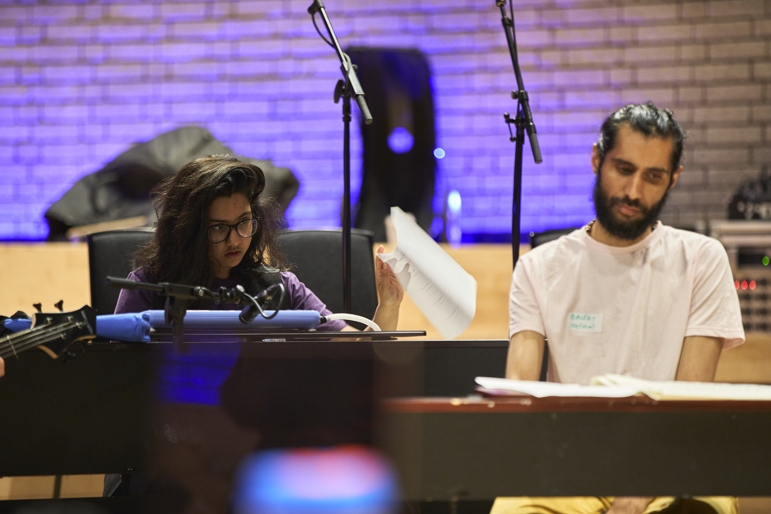 A young musician and Balraj Samrai sat behind a piano and a keyboard respectively looking down at the keys.