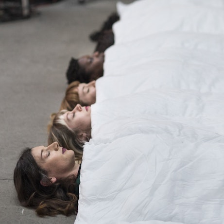 Residency artists lay in a row under an elongated quilt with their eyes shut.