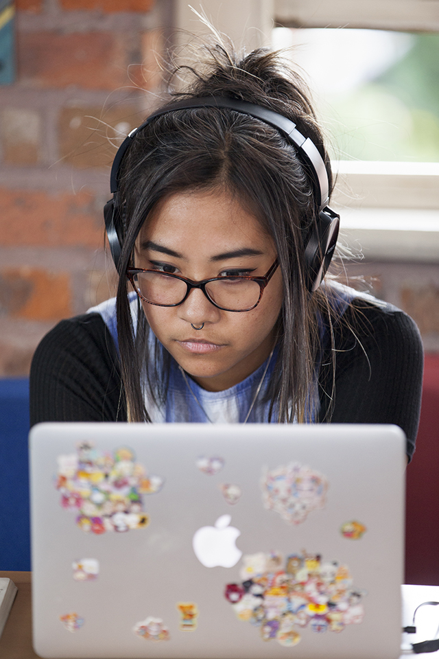 A visual artist on a laptop with headphones in.